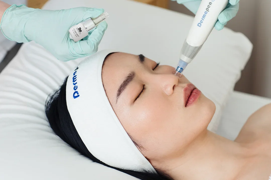 A woman lying on a treatment bed with a headband, receiving a facial injection from a healthcare professional using a syringe and a nasal spray.