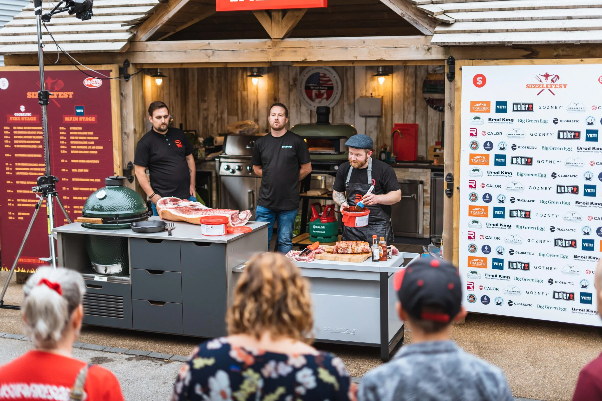Barbecue cooking demonstration at Sizzlefest with chefs preparing meat on outdoor grills, watched by an audience.