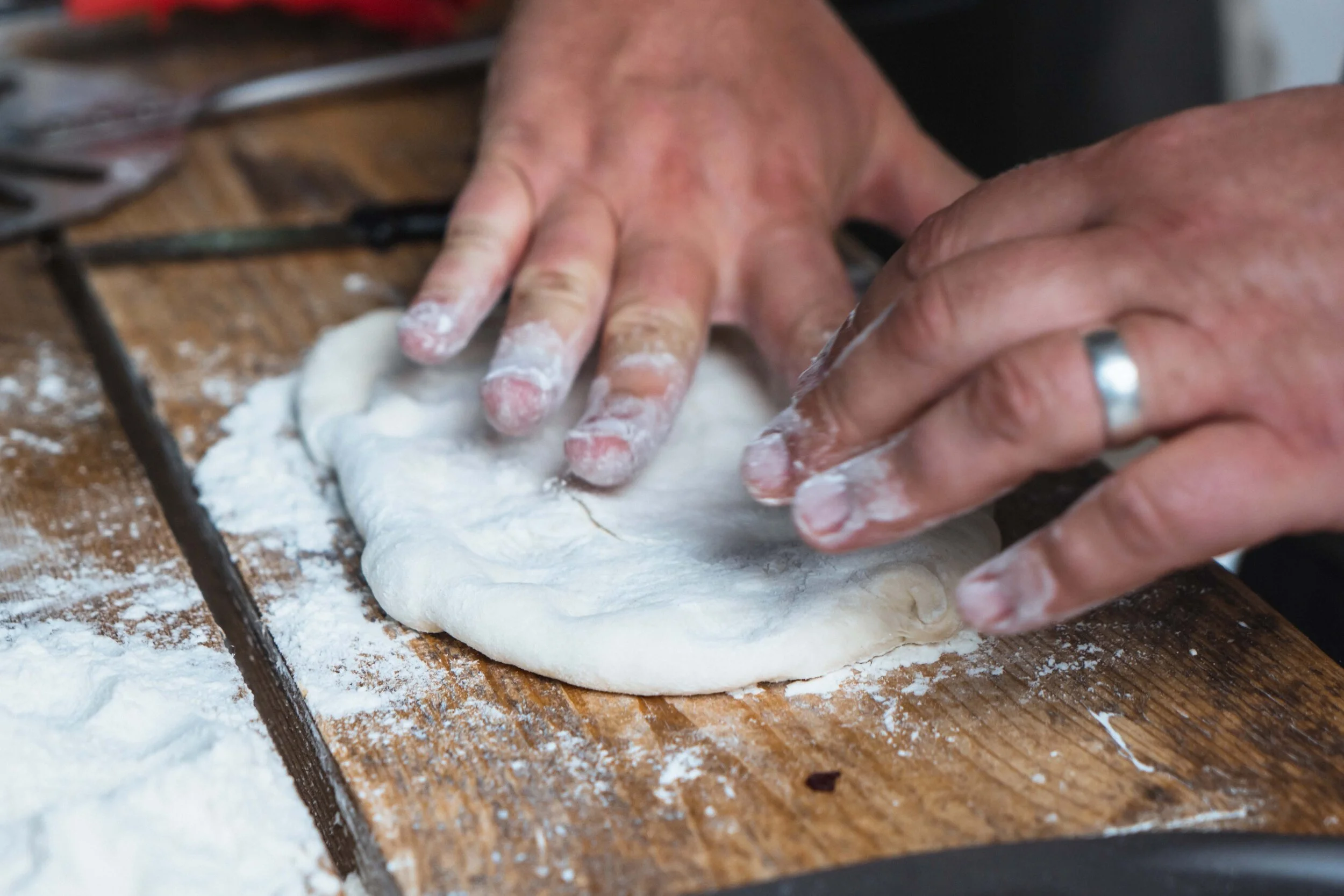 Hands preparing and shaping pizza dough on a floured wooden surface.