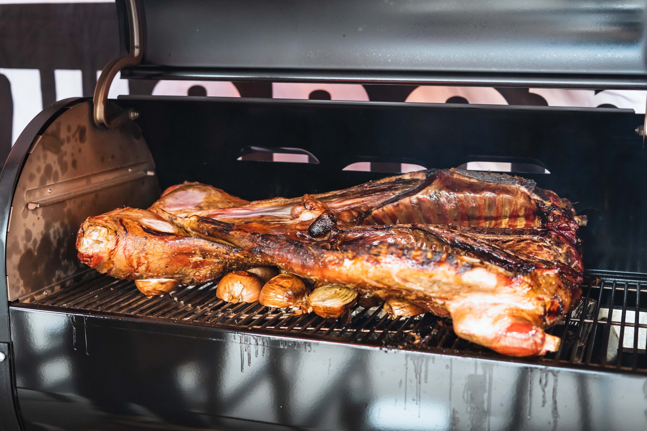 Grilled whole lamb on a barbecue smoker with onions underneath.