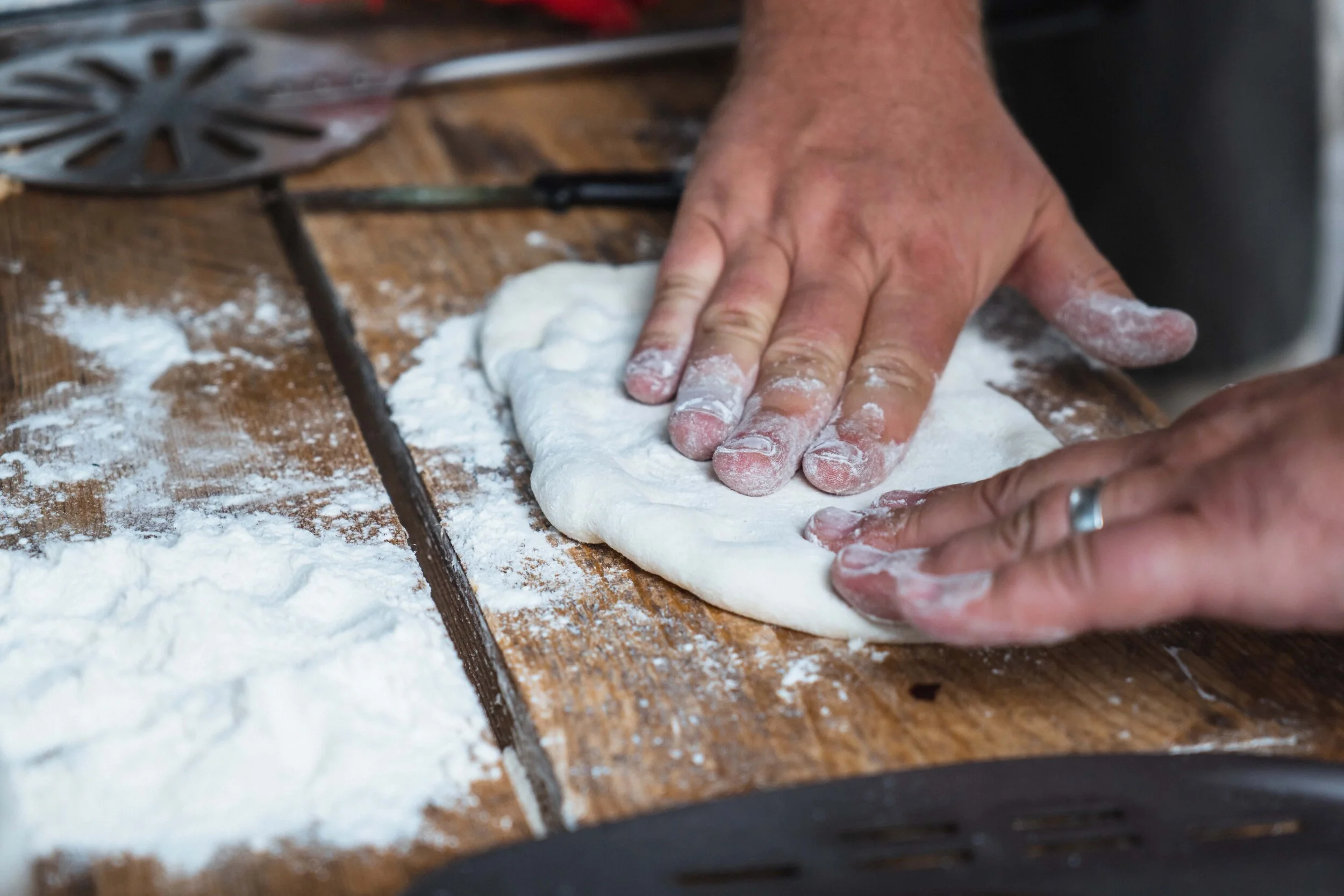 Hands kneading dough on a floured wooden surface for pizza or bread-making.