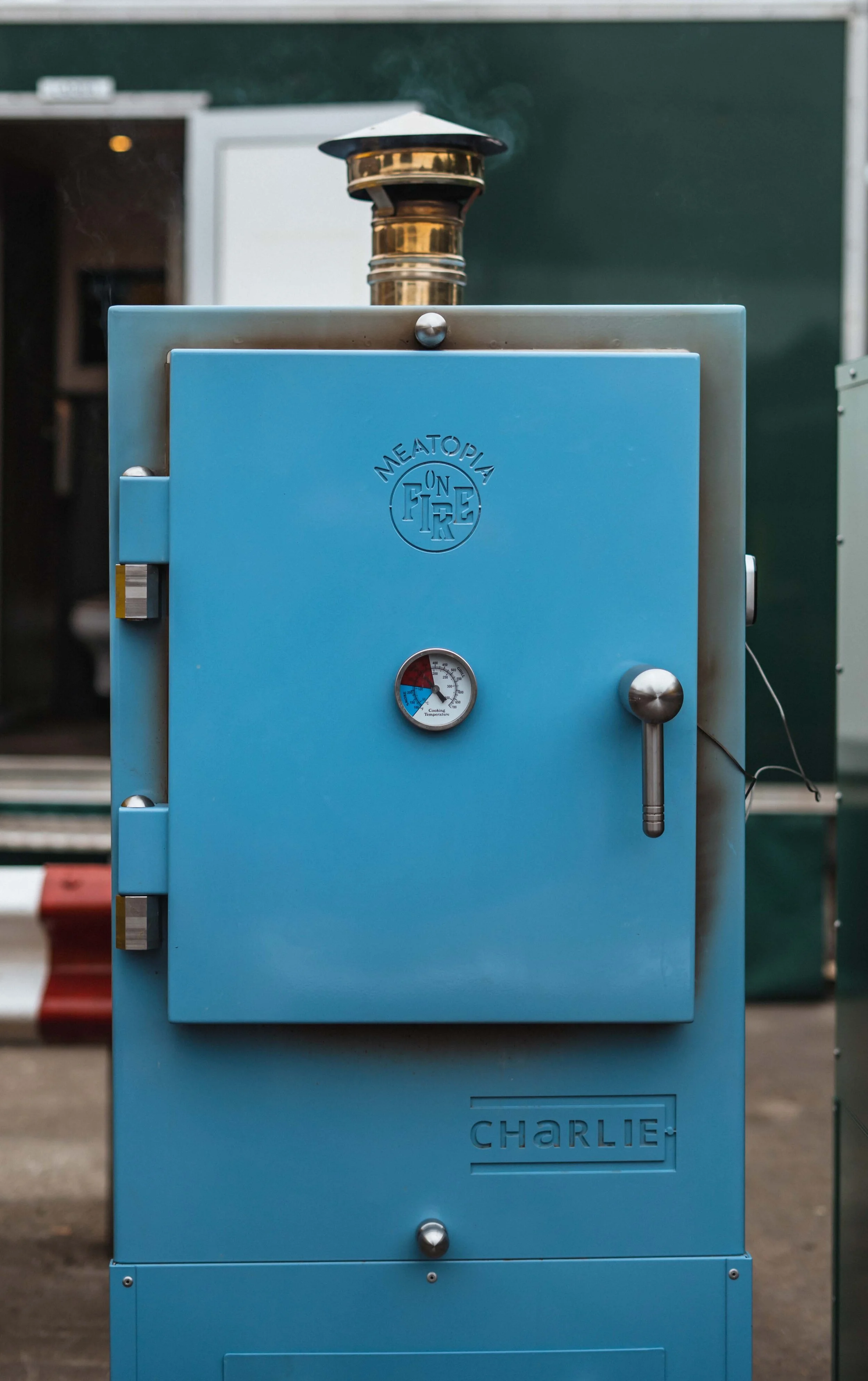 Blue outdoor smoker with temperature gauge and chimney, labeled "Meatopia" and "Charlie."