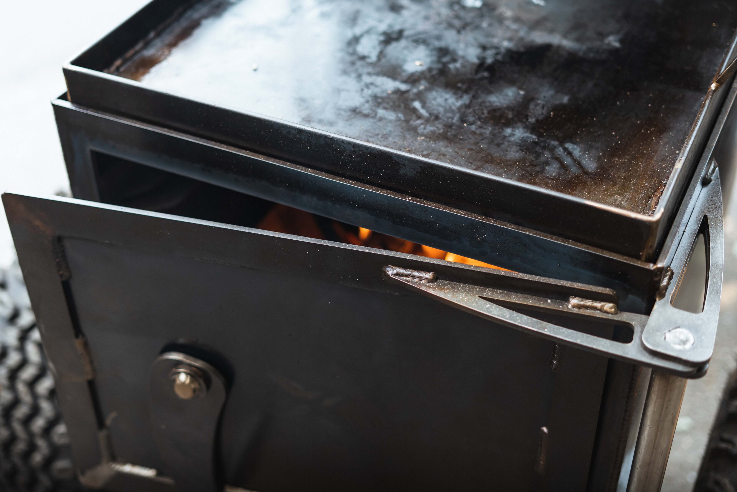 Open door of black wood stove with visible flames inside.