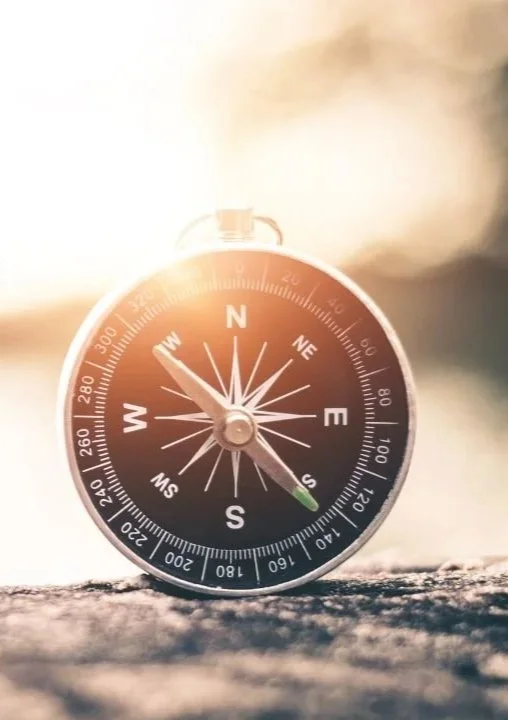 Close-up of a compass with a blurred natural background and sunlight.