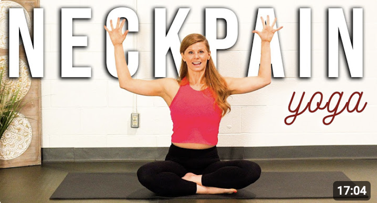 A woman with red hair in a pink tank top and black leggings sitting cross-legged on a yoga mat with arms raised in a yoga pose, in front of a wall with the large text 'NECK PAIN' and the word 'yoga' written in cursive.
