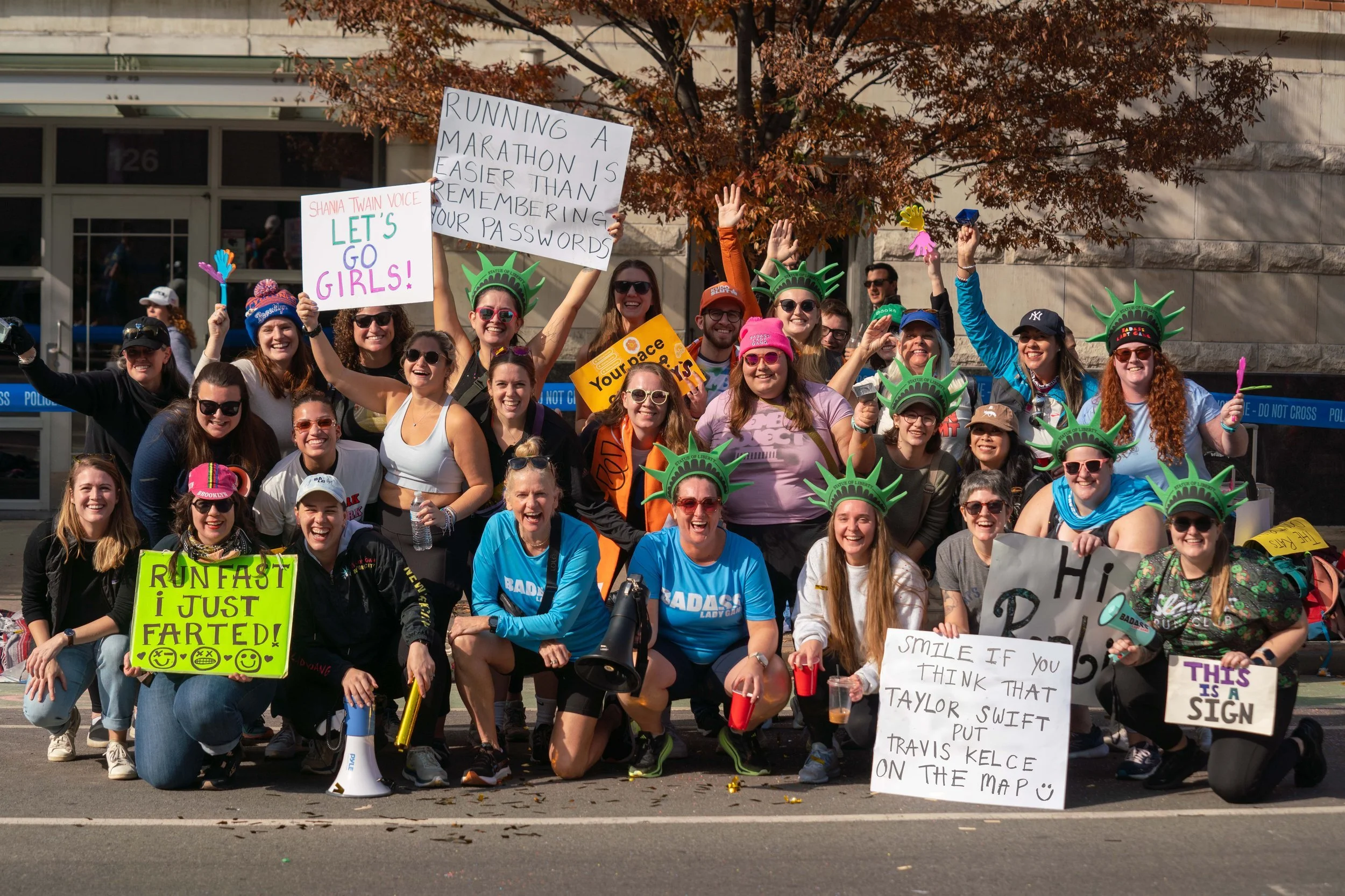 A big group of BALG women posing together at a race cheer zone with signs and green foam crowns