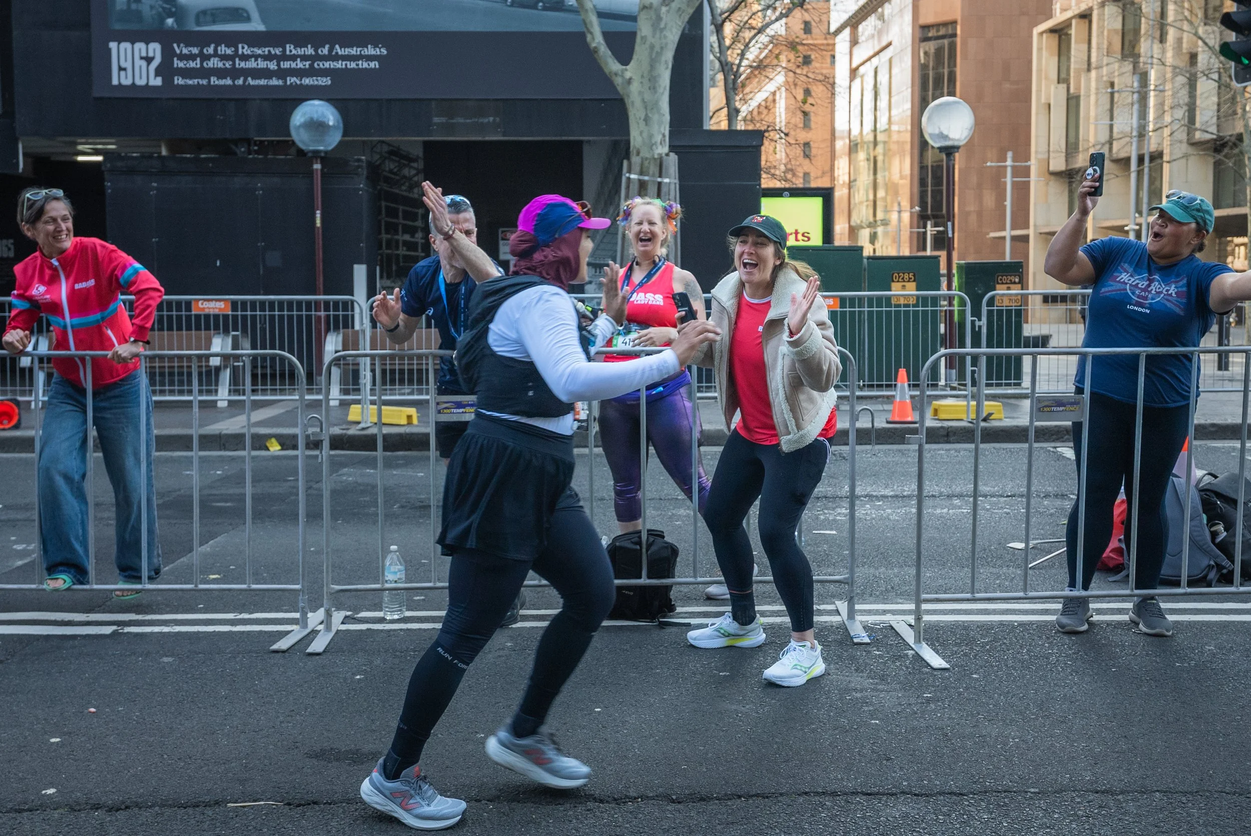 A runner dances past cheering supporters behind barricades at the Sydney Marathon