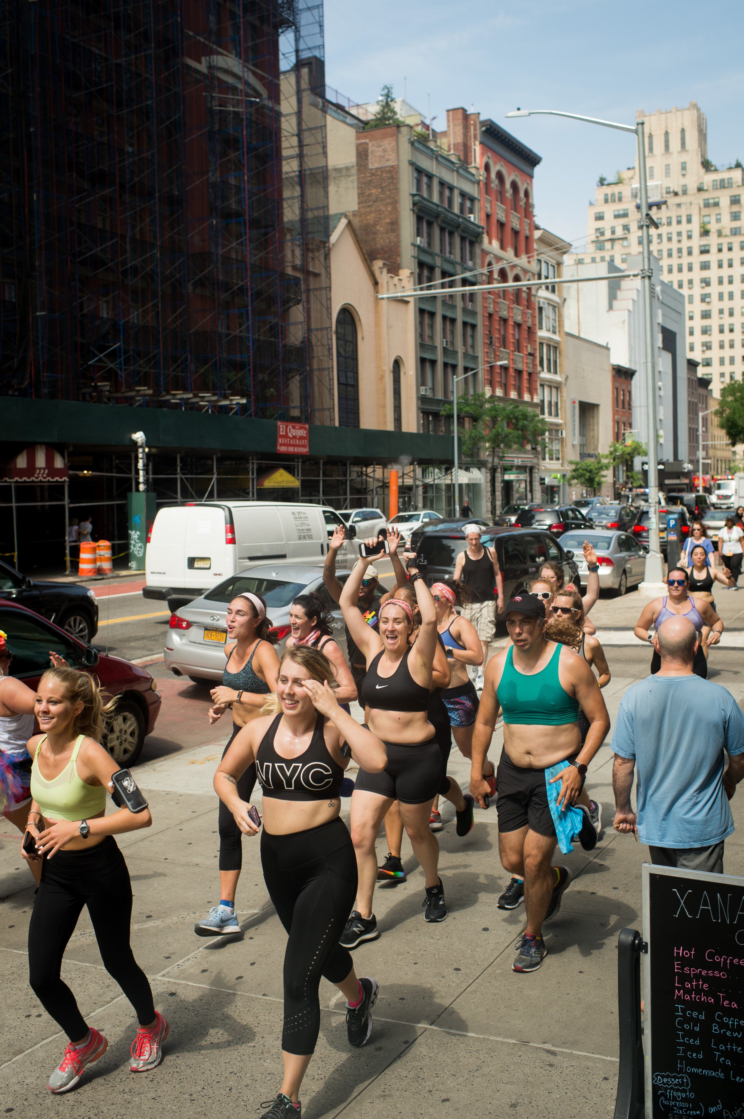 A group of women running together down a New York City street, smiling and cheering