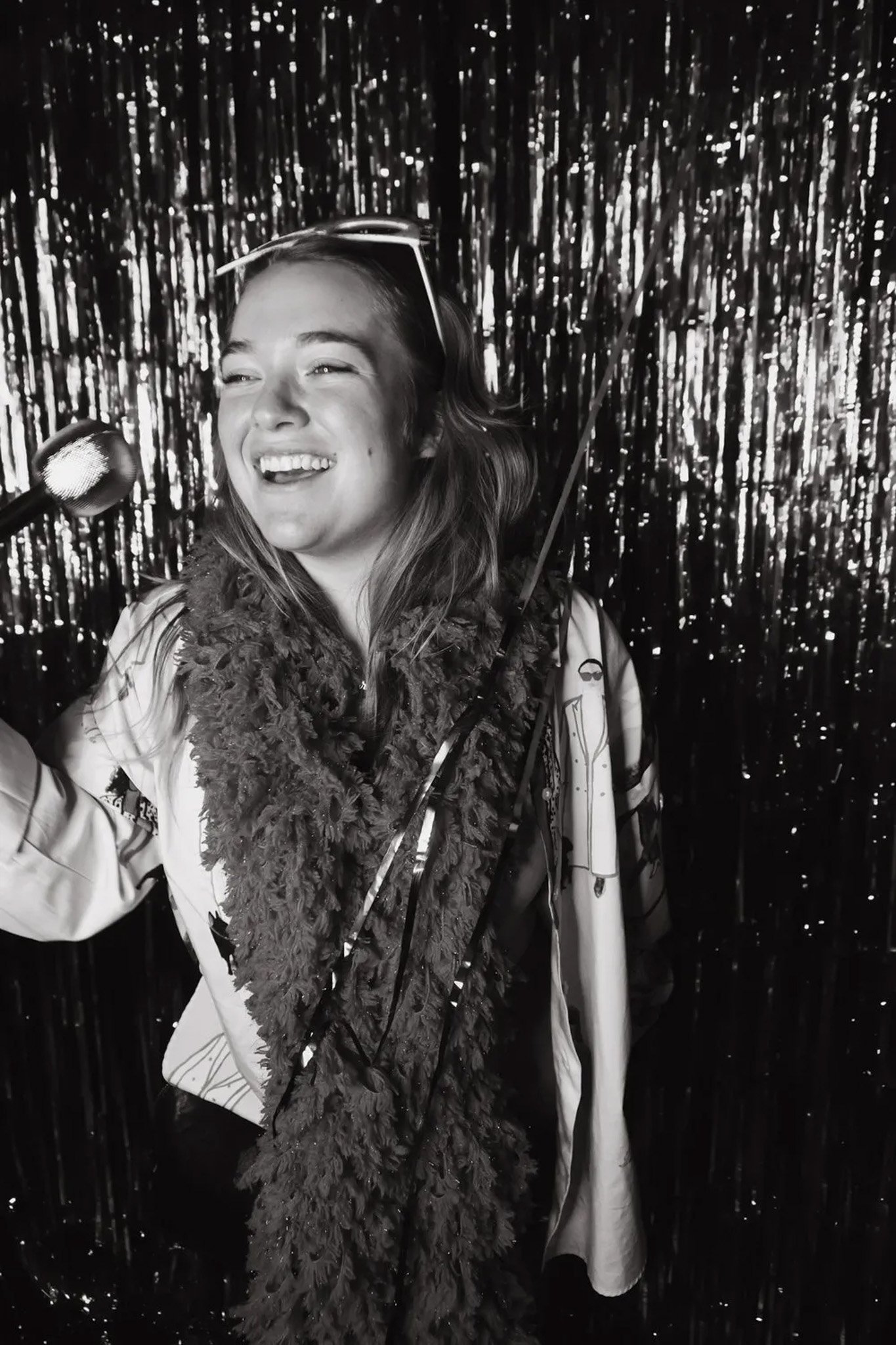 Smiling person with microphone and boa in front of shiny backdrop