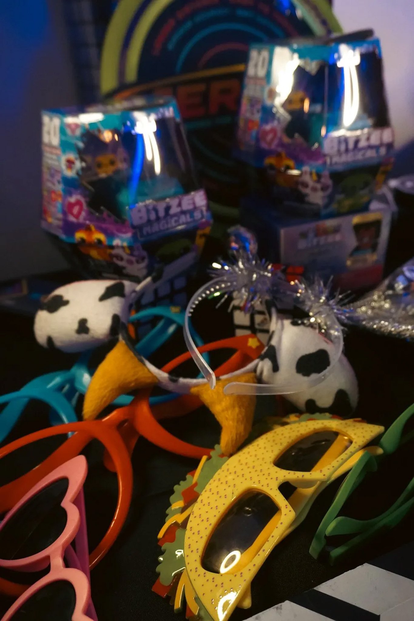 Colorful sunglasses, novelty headband with cow print and horns, and Bitzee Magical collectible boxes on a table.