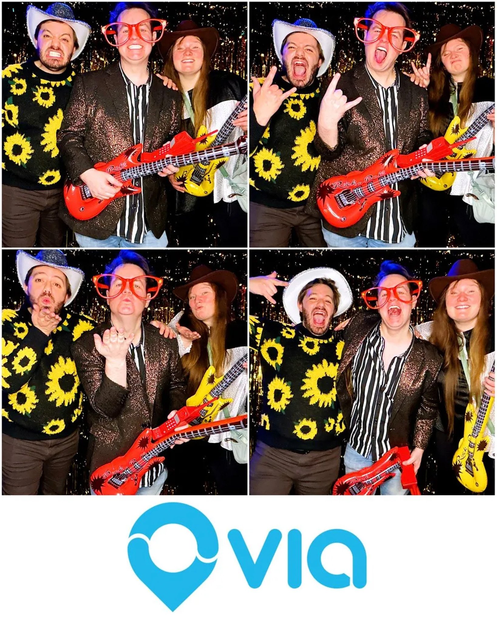Three people posing with props and costumes, including oversized glasses, a sparkling jacket, cowboy hats, a sunflower sweater, and inflatable guitars, in front of a decorative backdrop. A logo "Via" is displayed at the bottom.