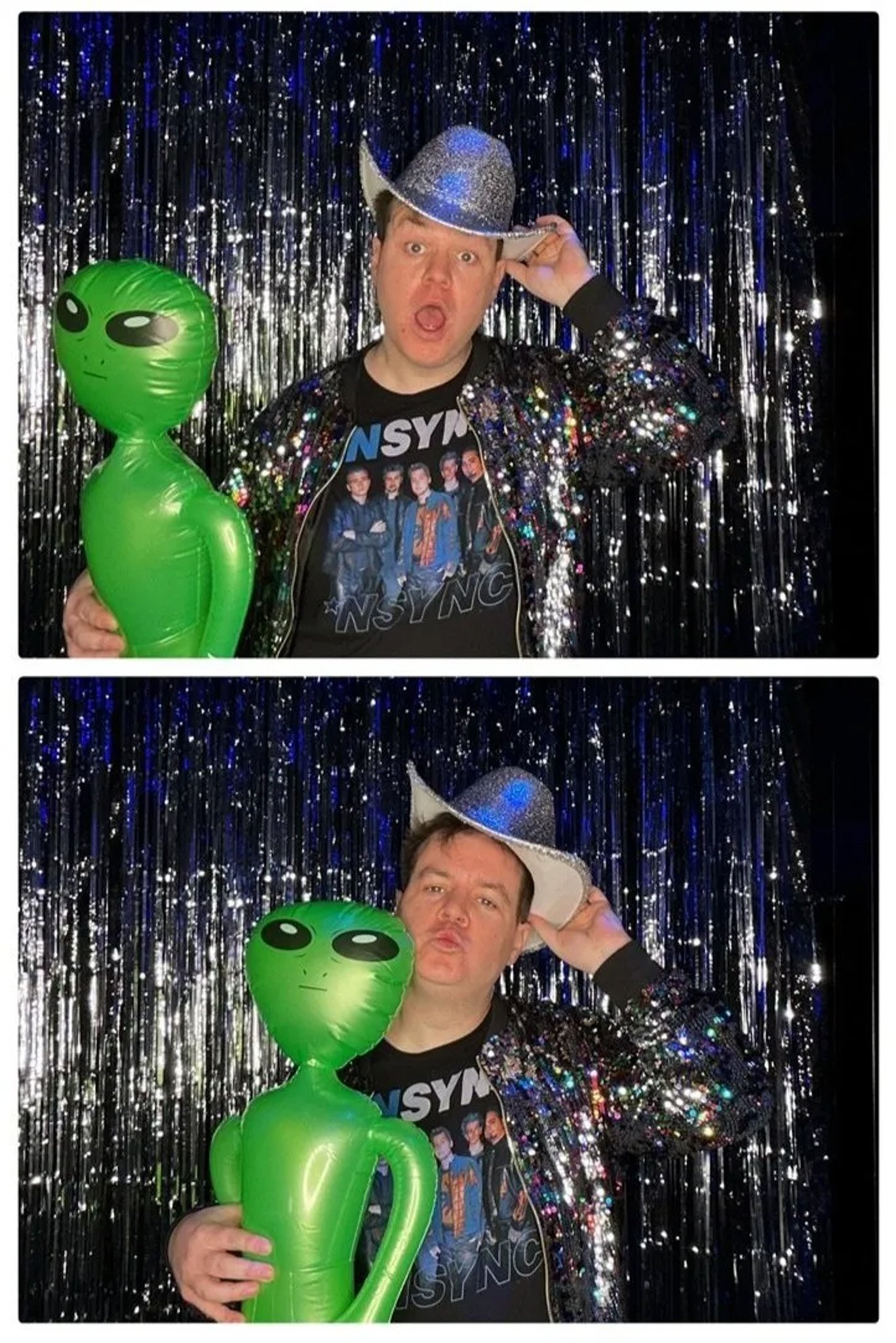 Person in a sparkly jacket and hat with a green inflatable alien in front of a glittery backdrop.