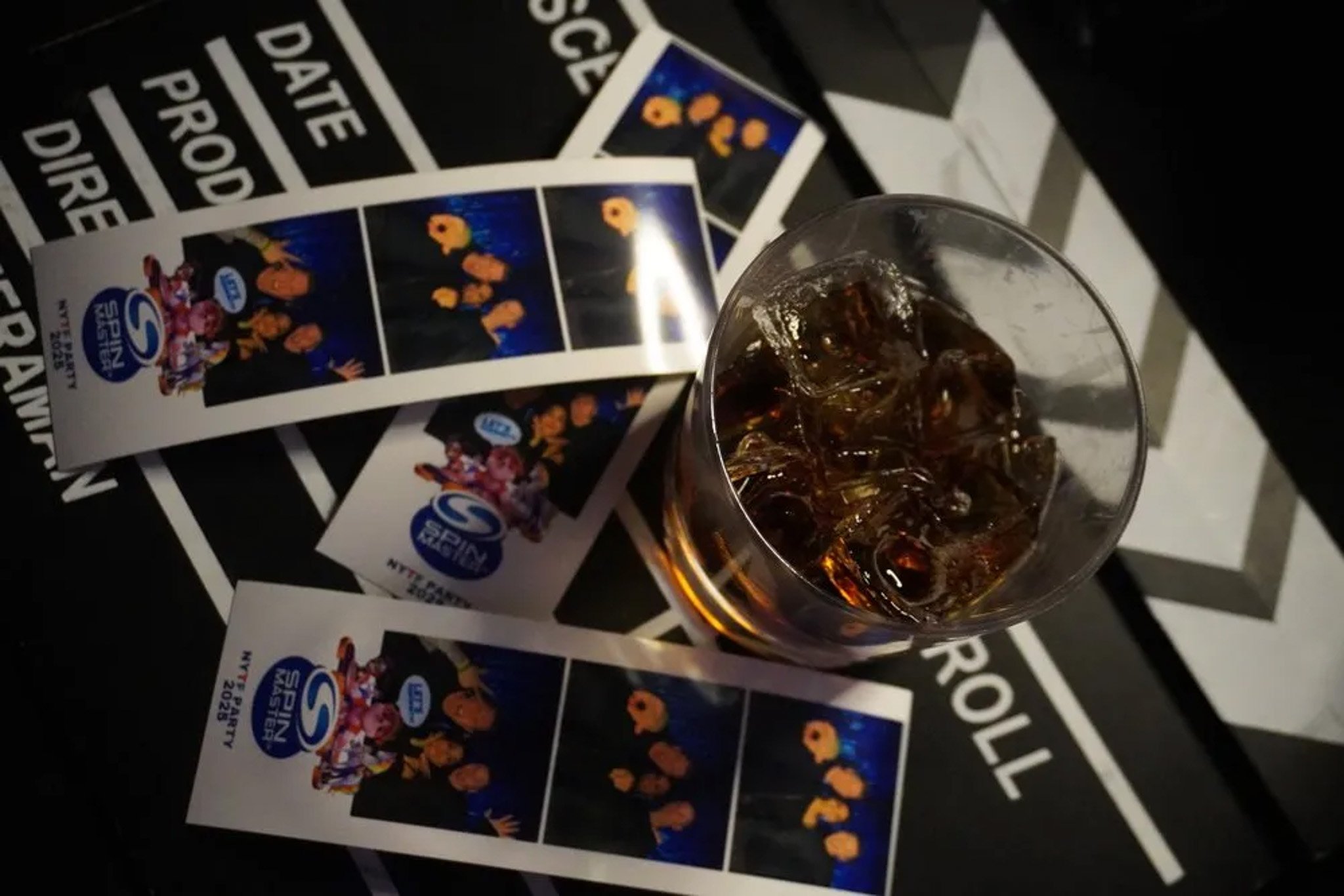 Photo booth strips on a clapperboard with a glass of soda and ice.