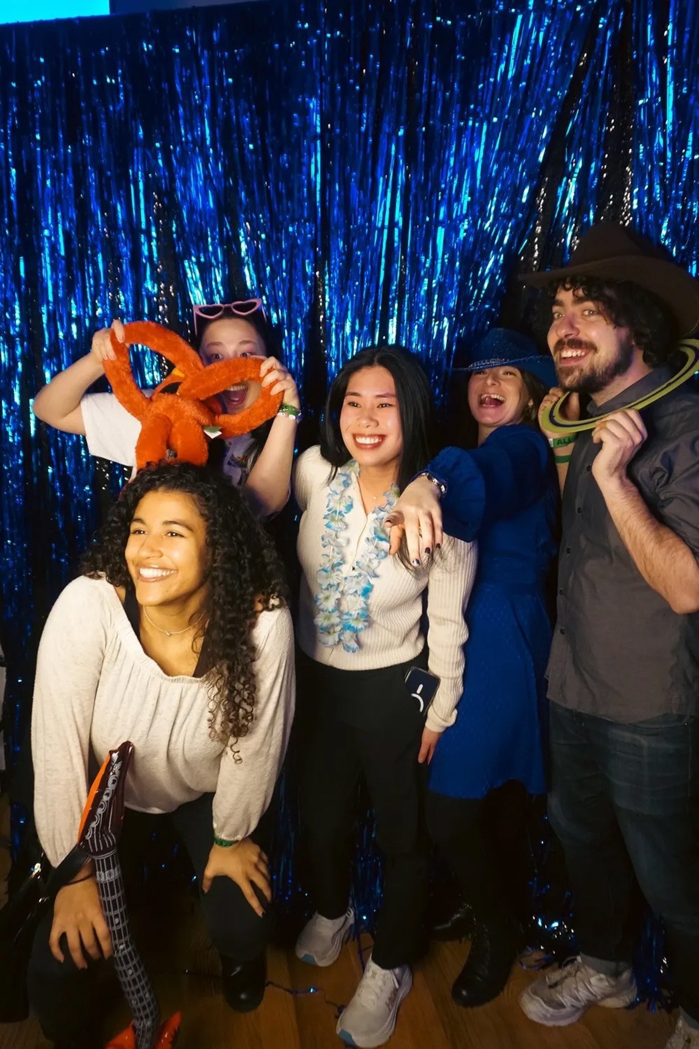 Group of people having fun at a party with props and blue tinsel backdrop.
