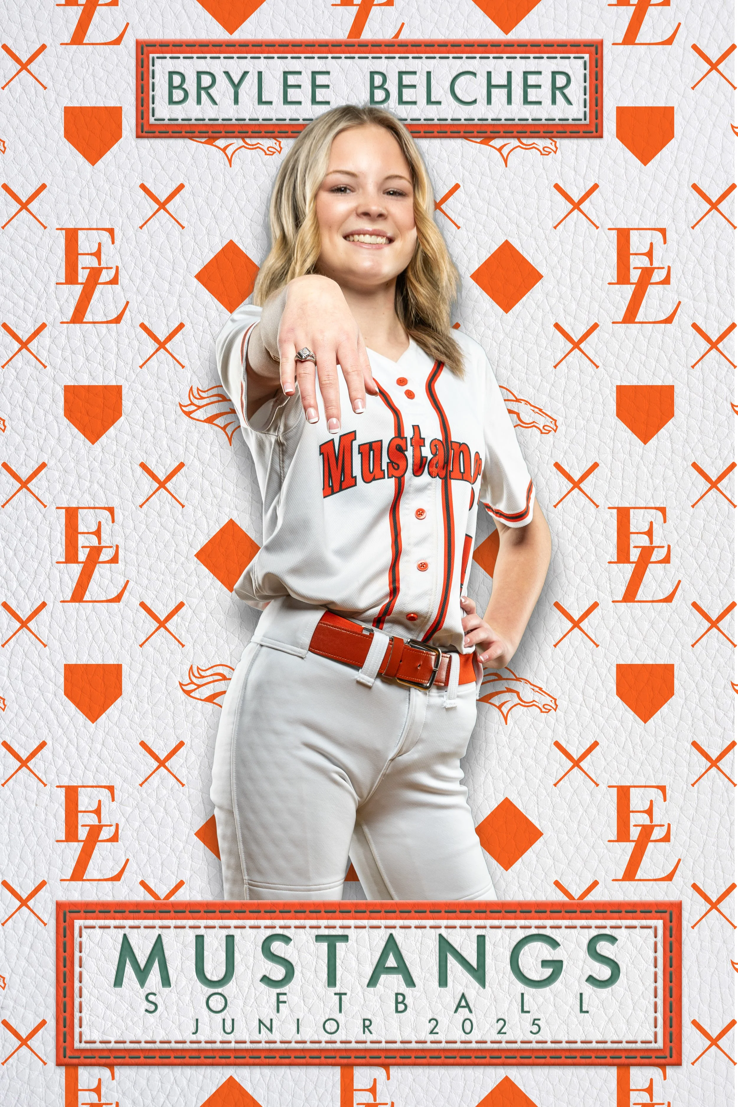 Young woman in a white softball uniform with orange and black accents, posing with a confident smile and demonstrating a ring on her finger, standing in front of a backdrop with the repeat words 'FE' and orange shield logos, and a sign that reads 'Br