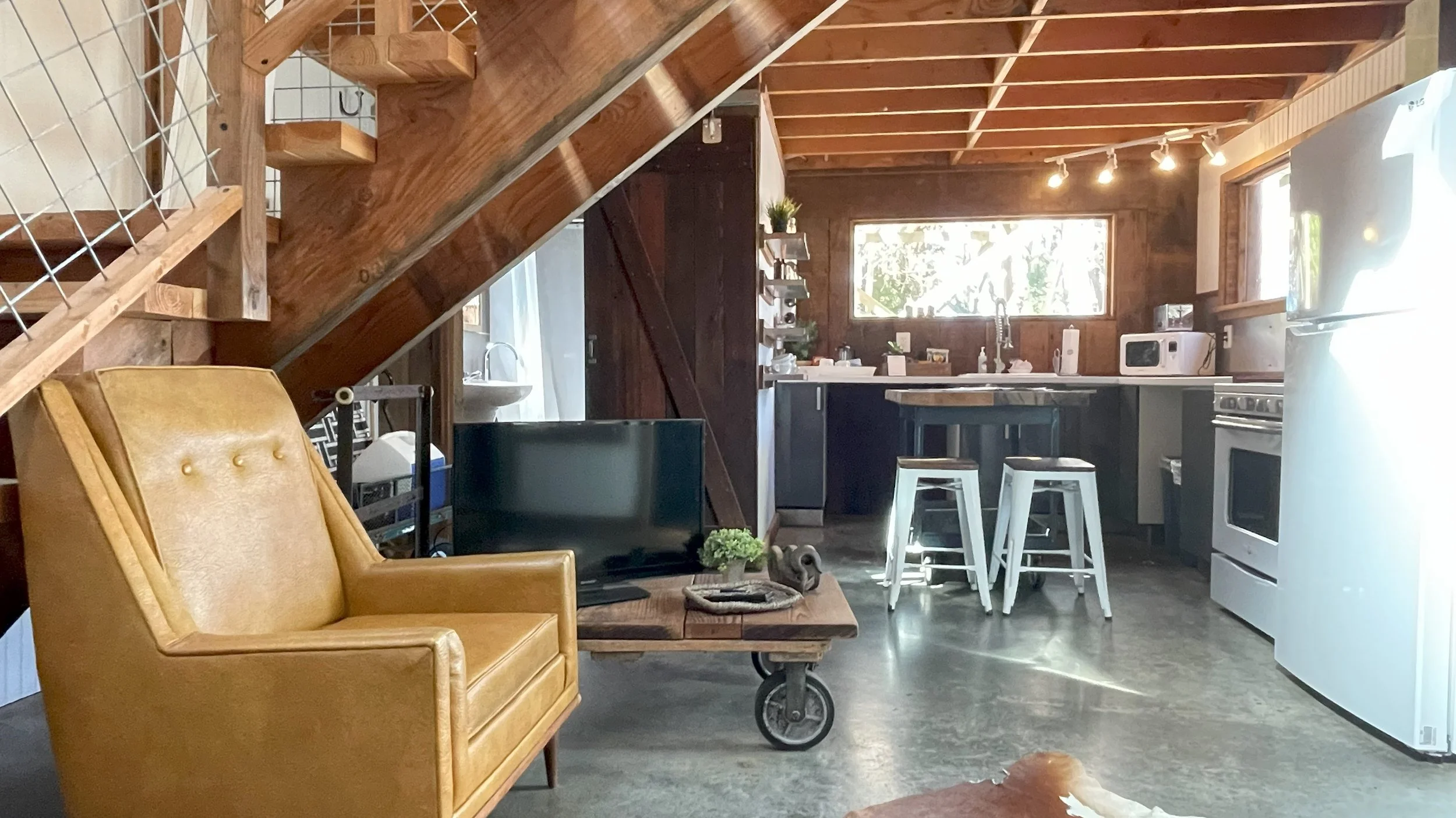 Rustic cabin interior with a mustard leather armchair, wooden staircase, industrial coffee table and open kitchen