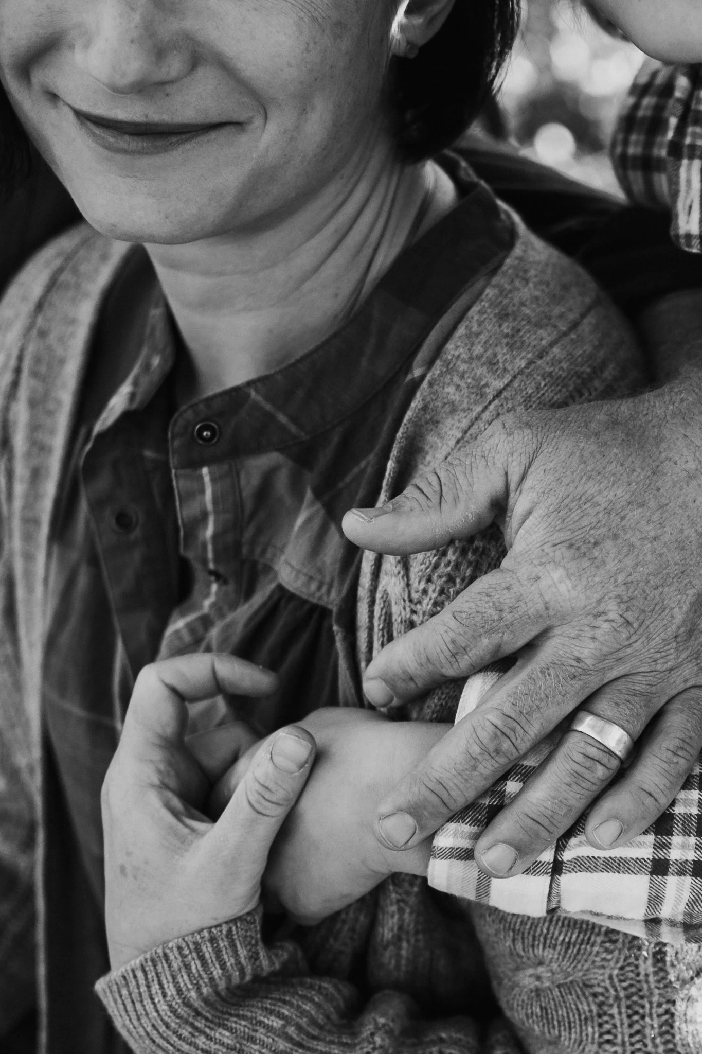 A woman smiling while gently holding and touching a child's hand, with their arms around each other, in a close-up black-and-white photo.