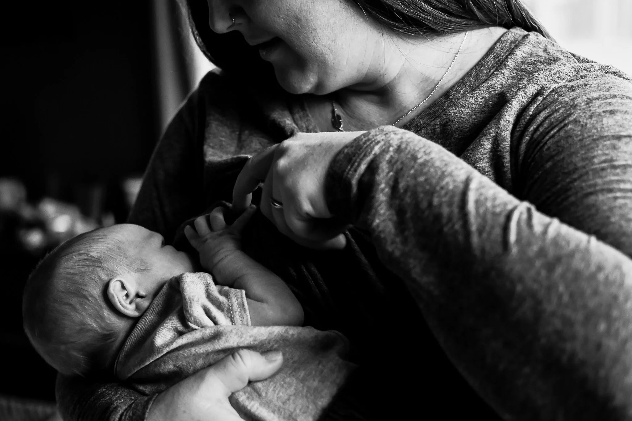 A woman holding and breastfeeding a newborn baby in a close-up black-and-white photograph.