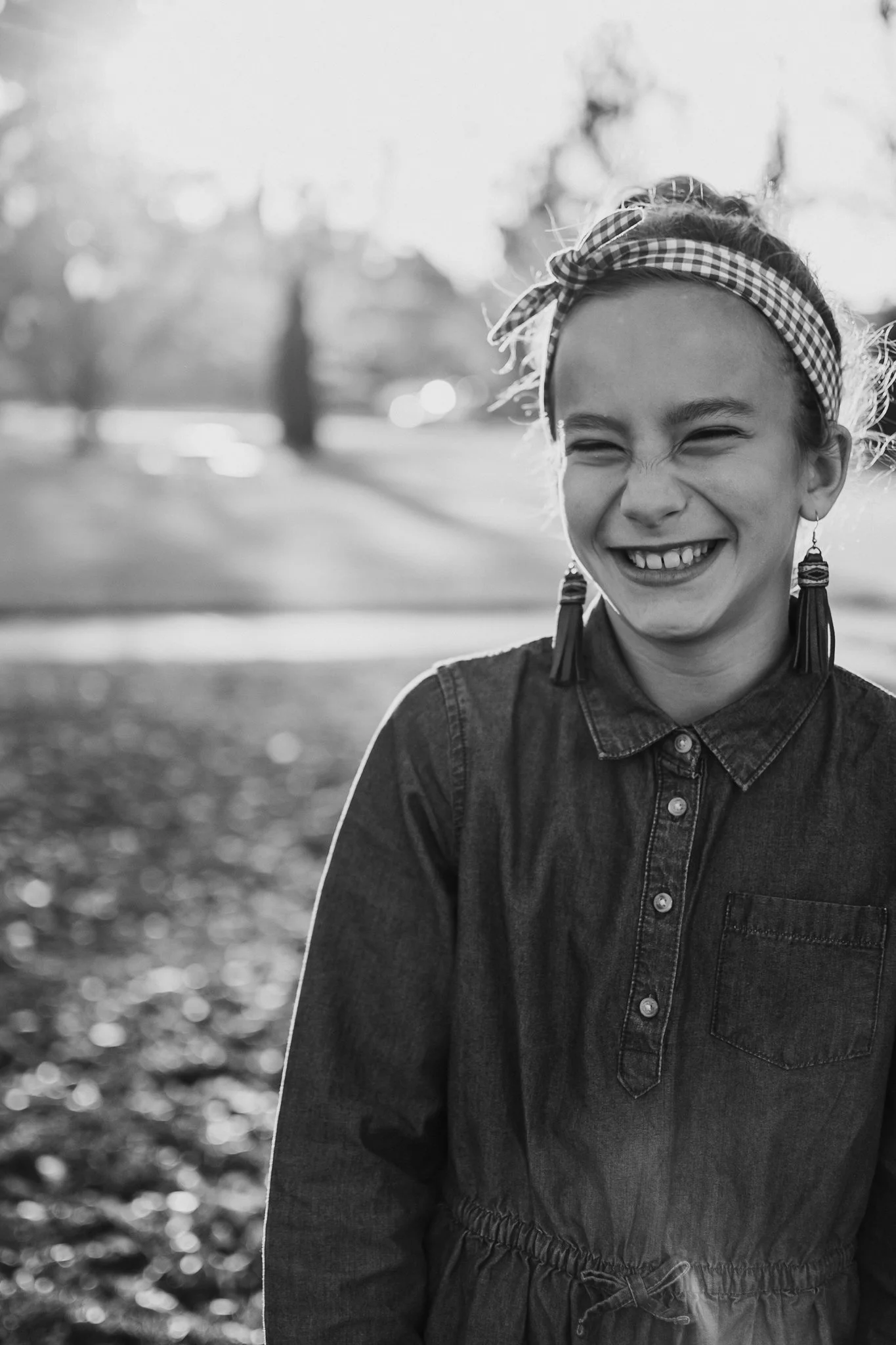Black and white photo of a girl smiling outdoors, wearing a headband, earrings, and a denim jacket.