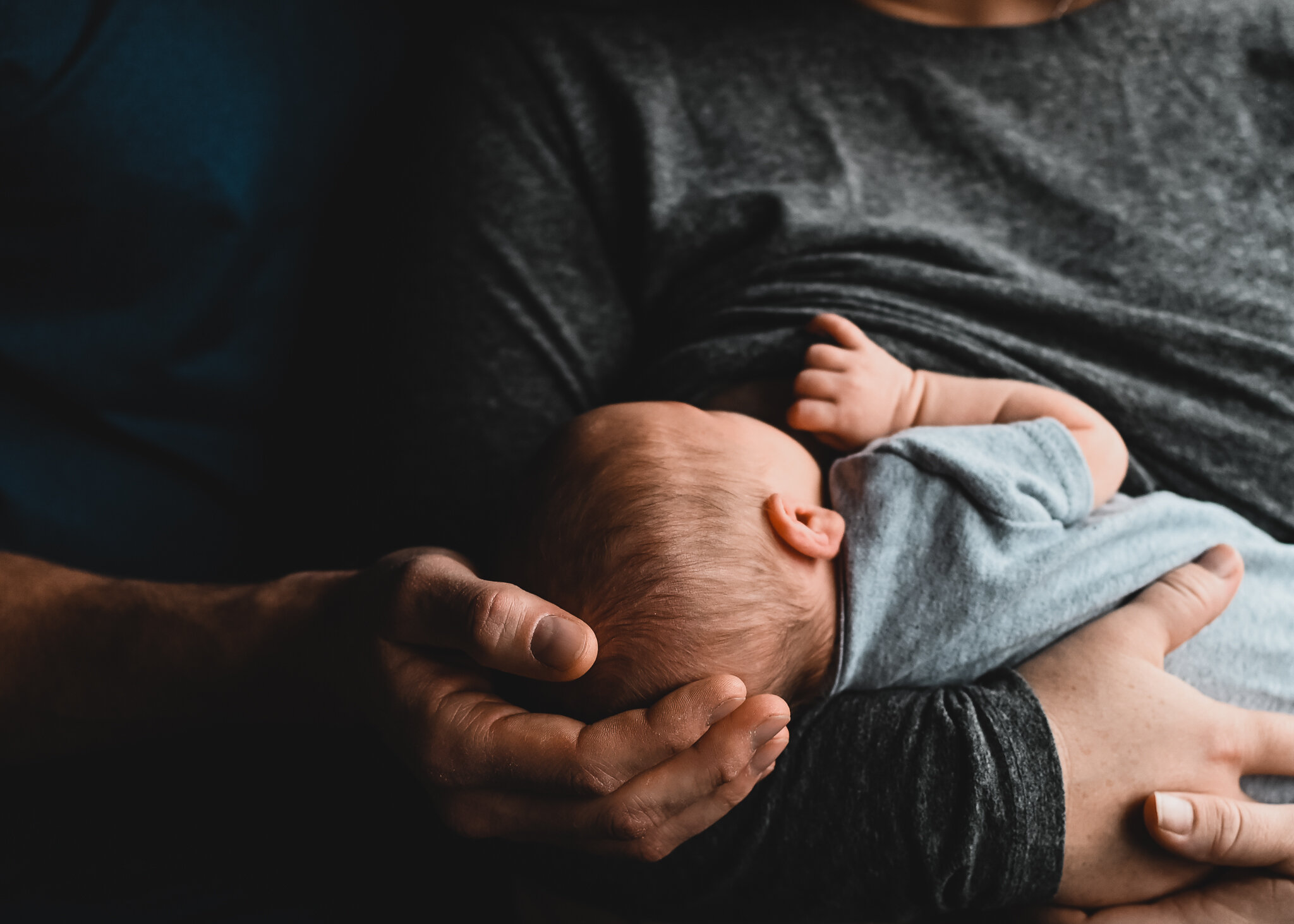 A baby lying on an adult's chest, being held gently with one hand supporting the baby's head and the other hand resting on the adult's chest.