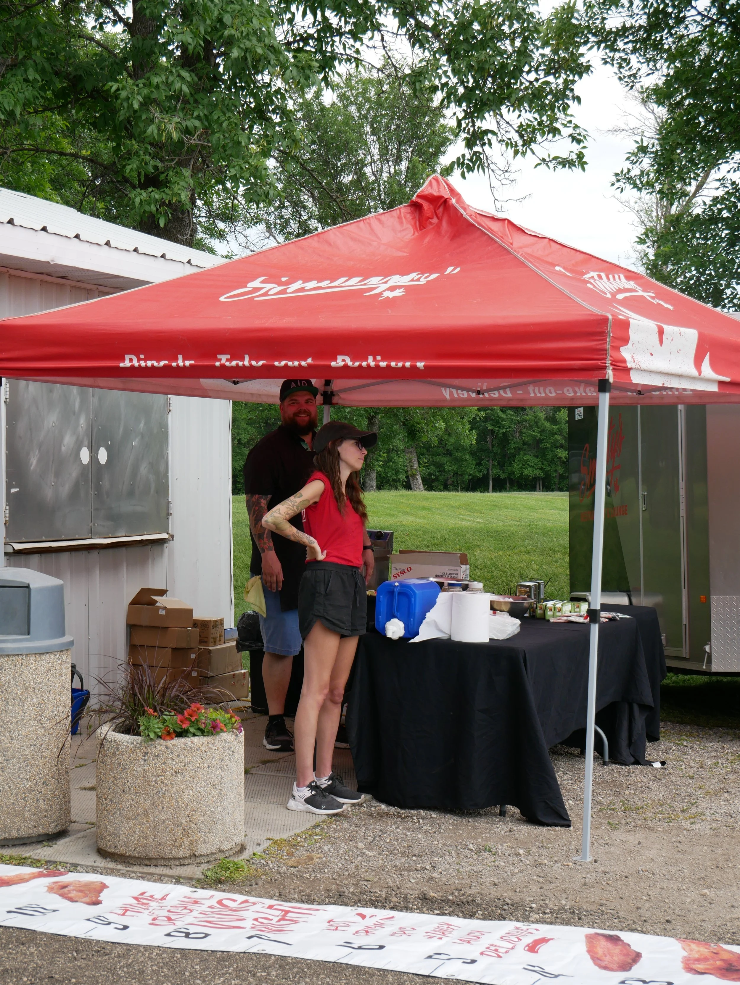 A man and a woman standing under a red canopy with white and red writing.
