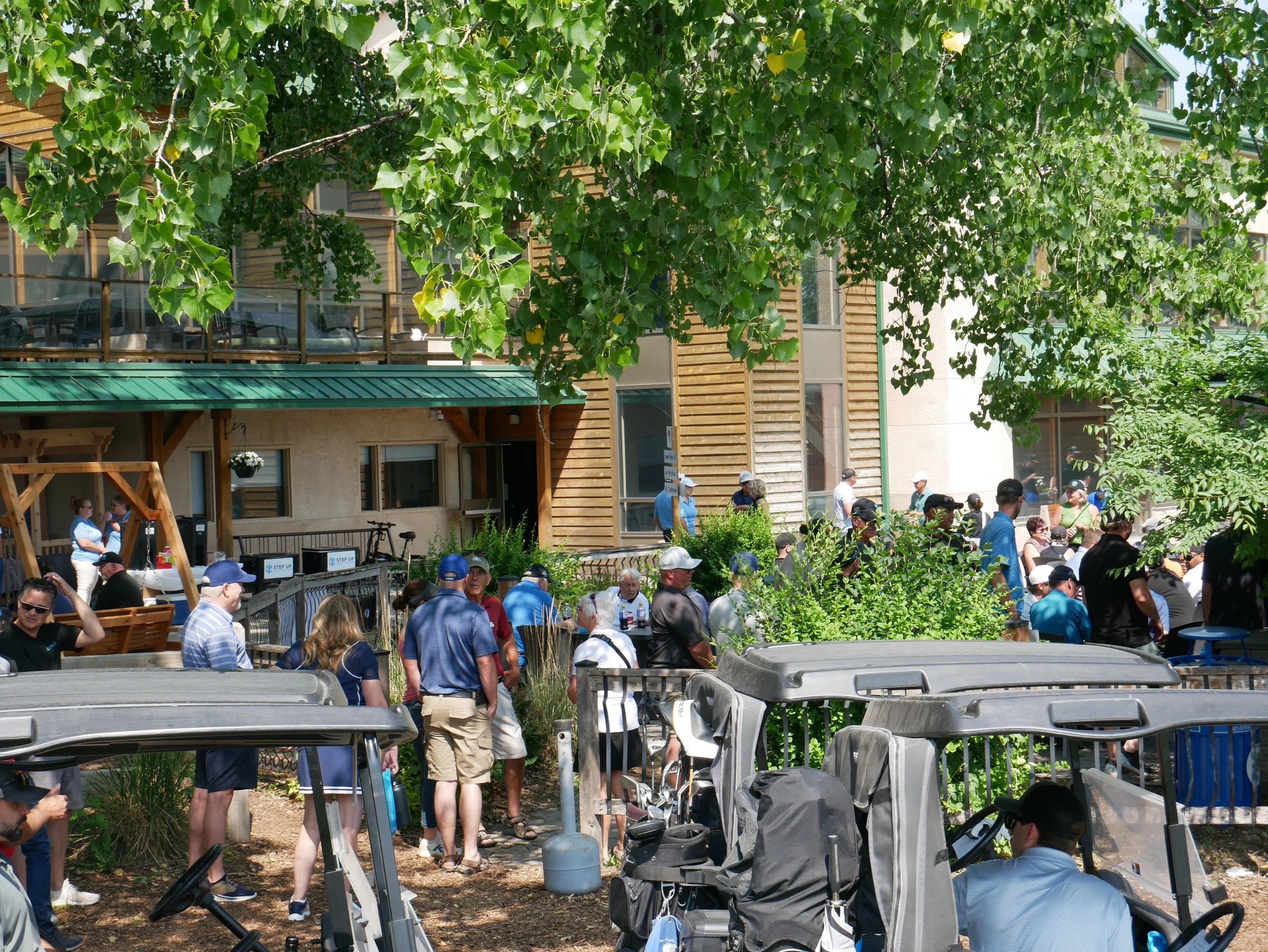 People gathering outdoors near a building with green trees and carts.