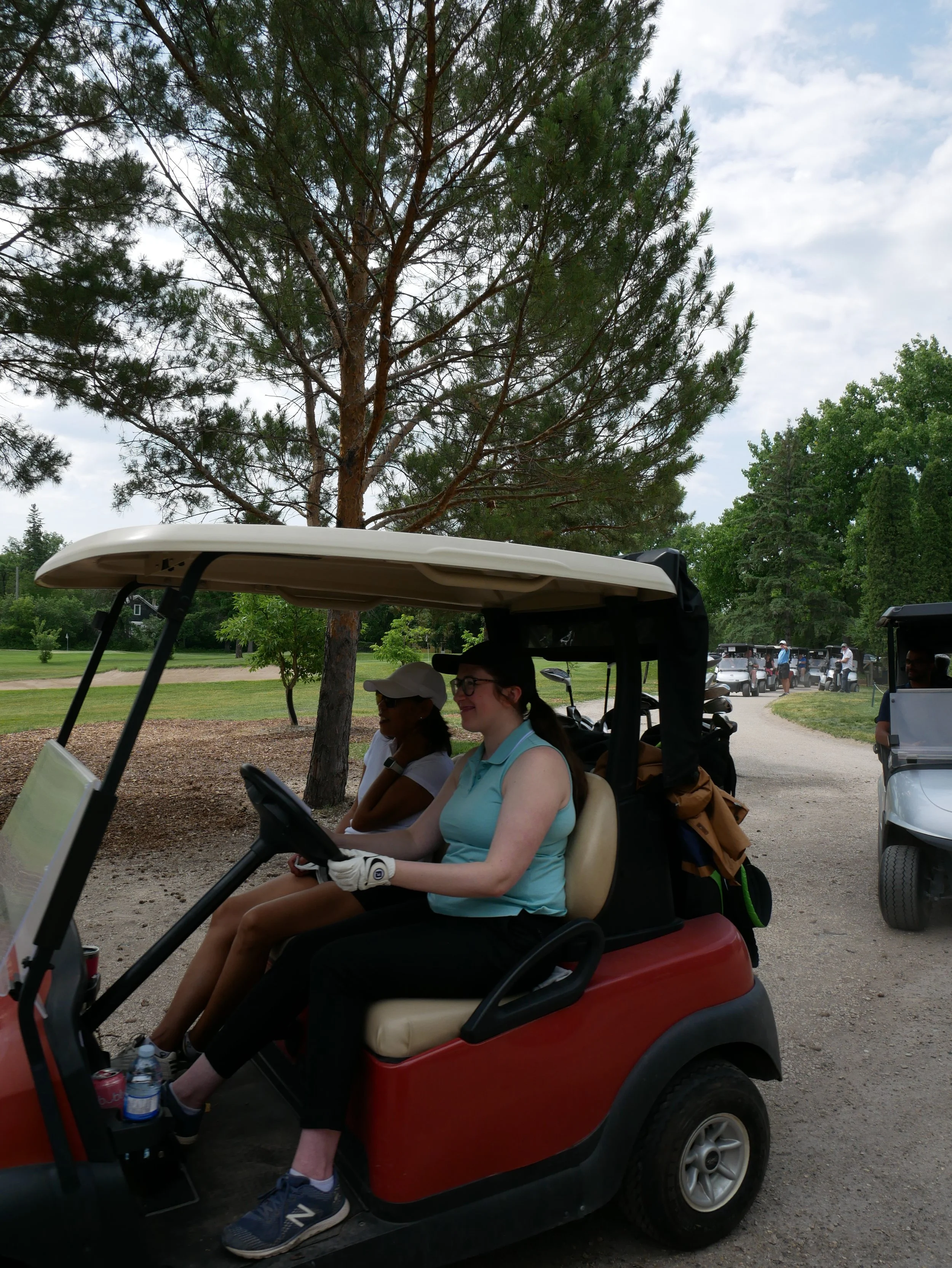 People riding in a golf cart on a golf course with trees and a path in the background.