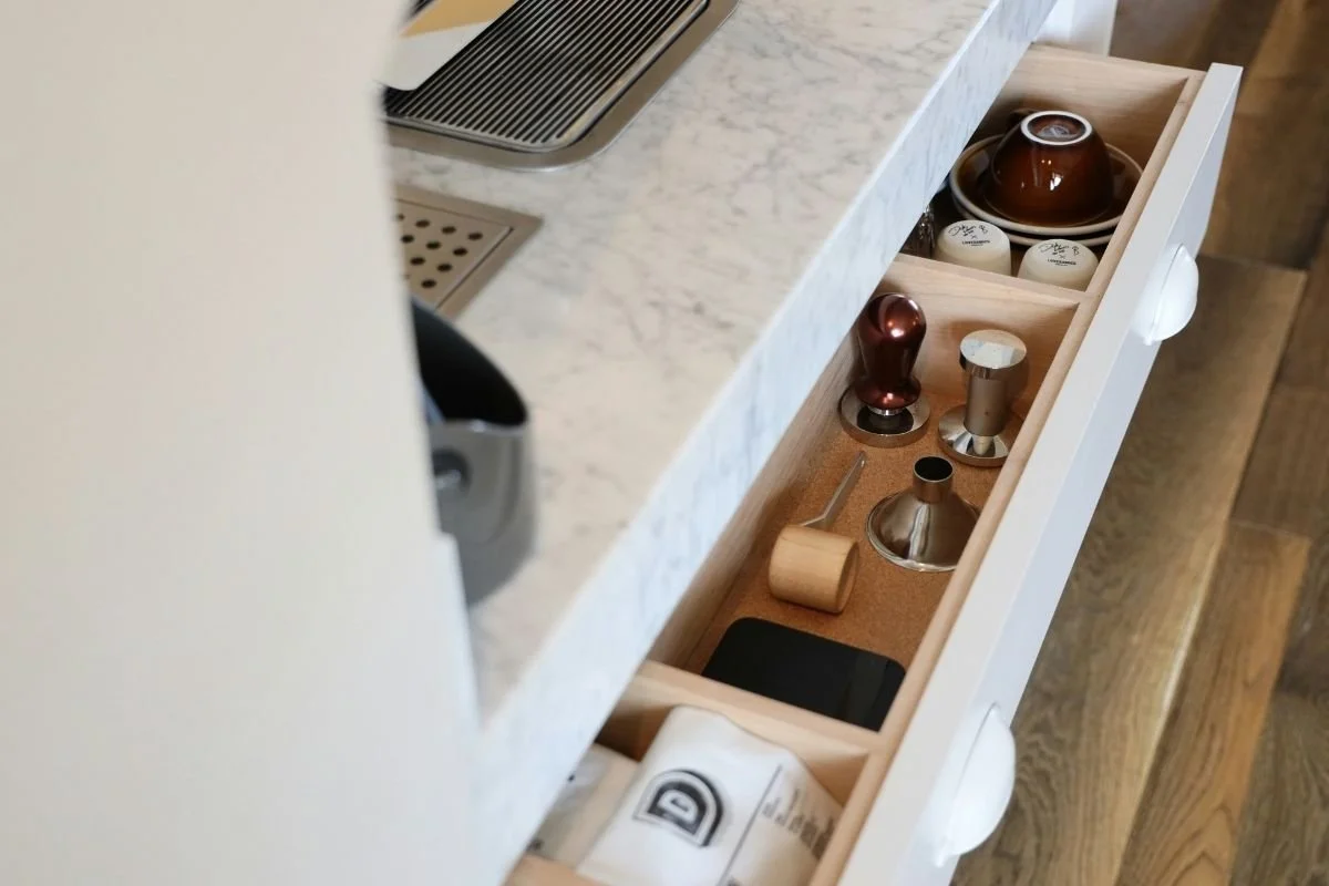 A series of pots, mugs, and coffee-making utensils in a long kitchen drawer.