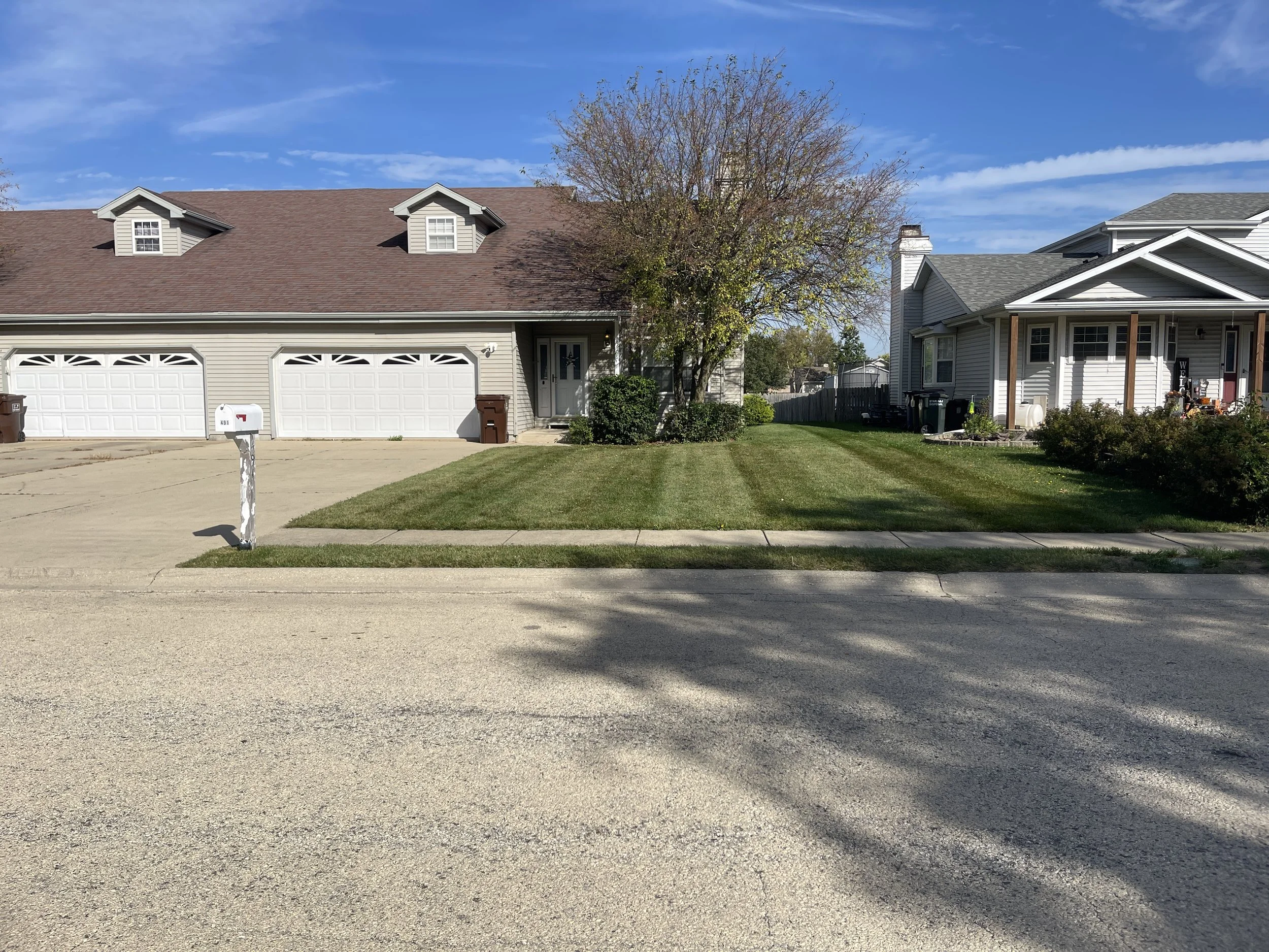 Freshly mowed residential front lawn in Manteno, Illinois, with mowing lines between the driveway and neighboring property.