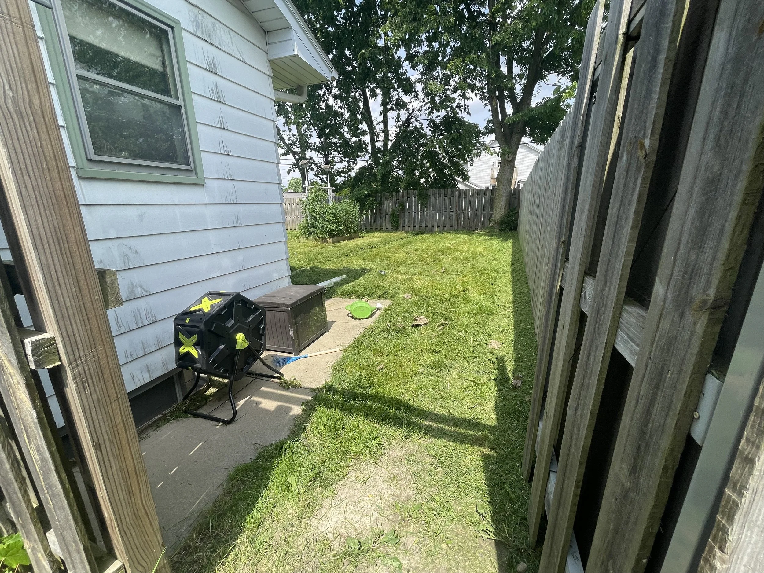 The same backyard entrance after mowing, showing shorter grass beside the concrete walkway.