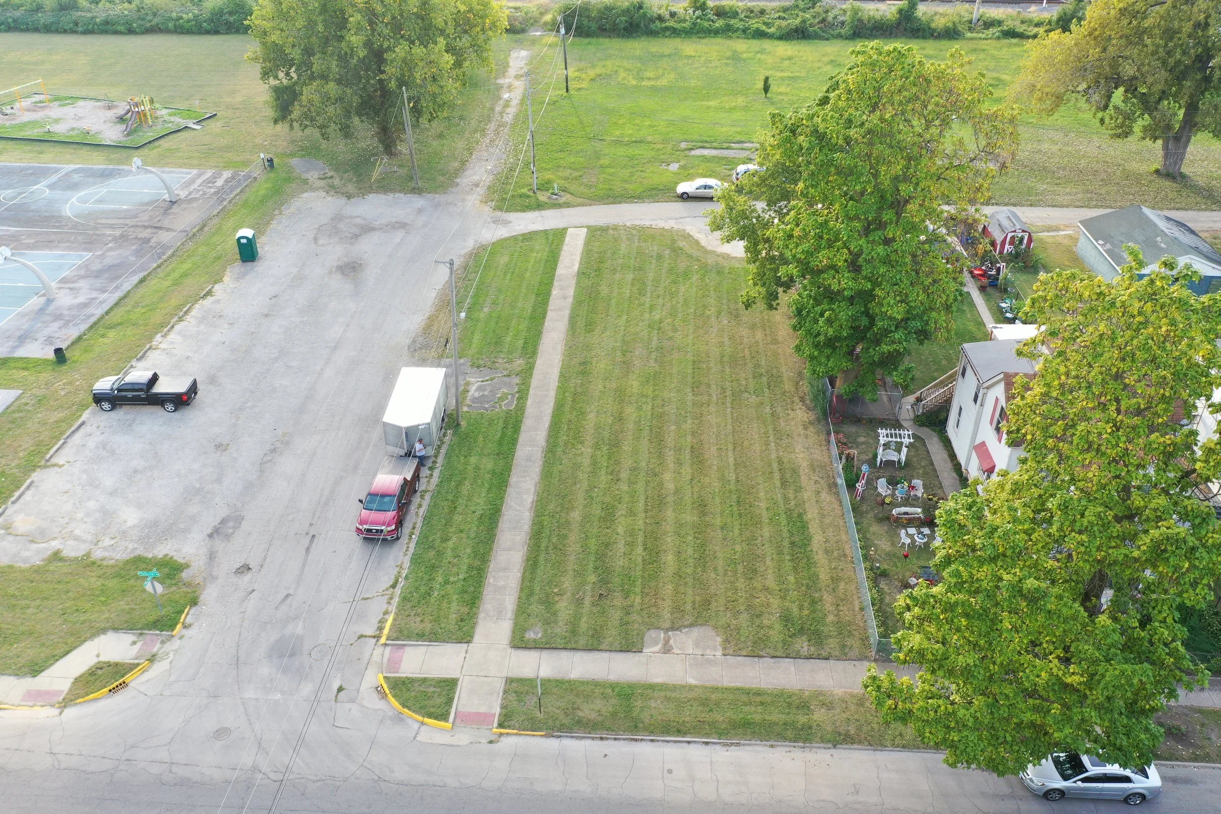 Aerial view of a freshly mowed vacant lot in Kankakee, Illinois, with mowing lines visible beside the sidewalk.