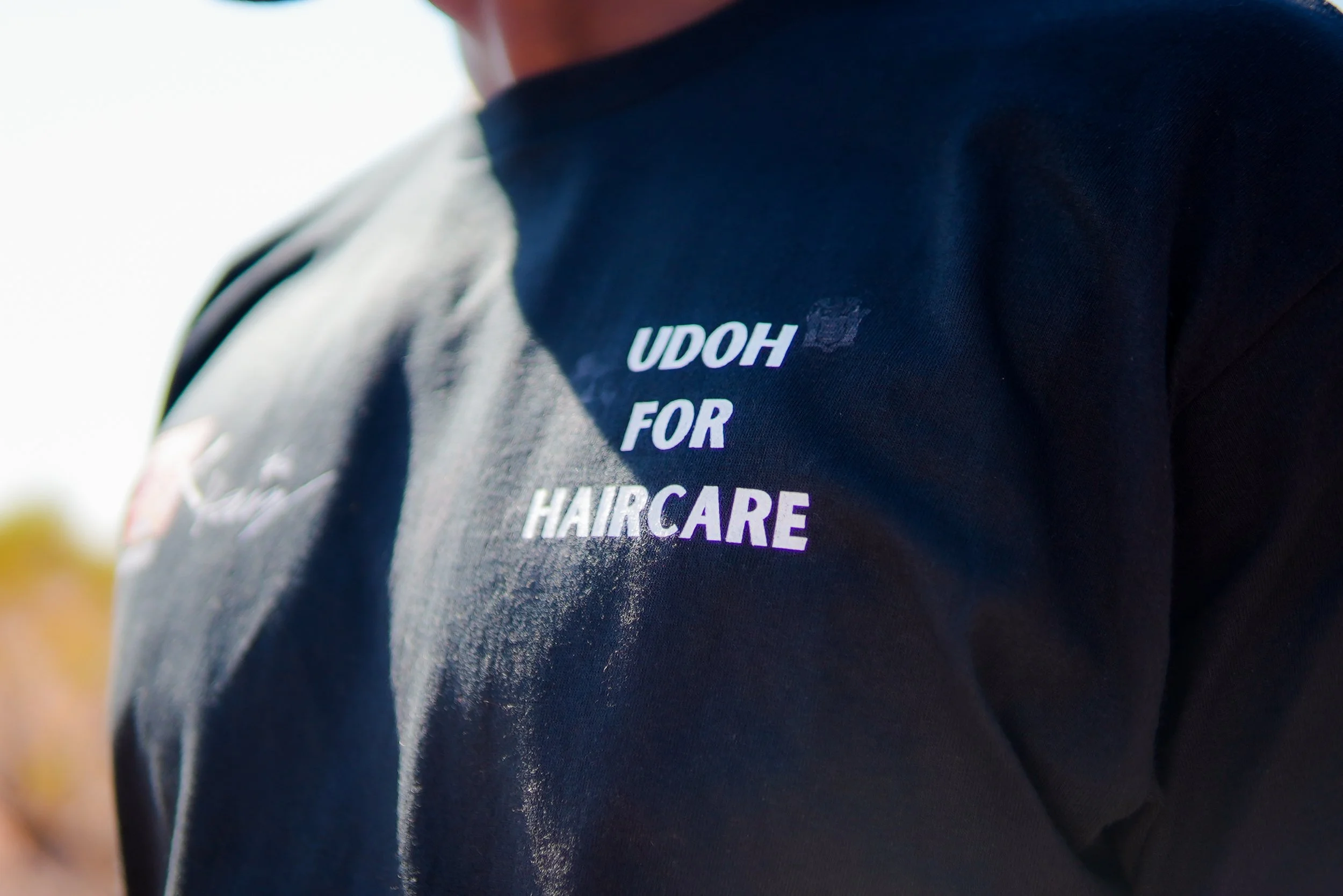 Close-up of a person wearing a dark jacket with purple and white text reading 'UDOH FOR HAIRCARE' on the back.