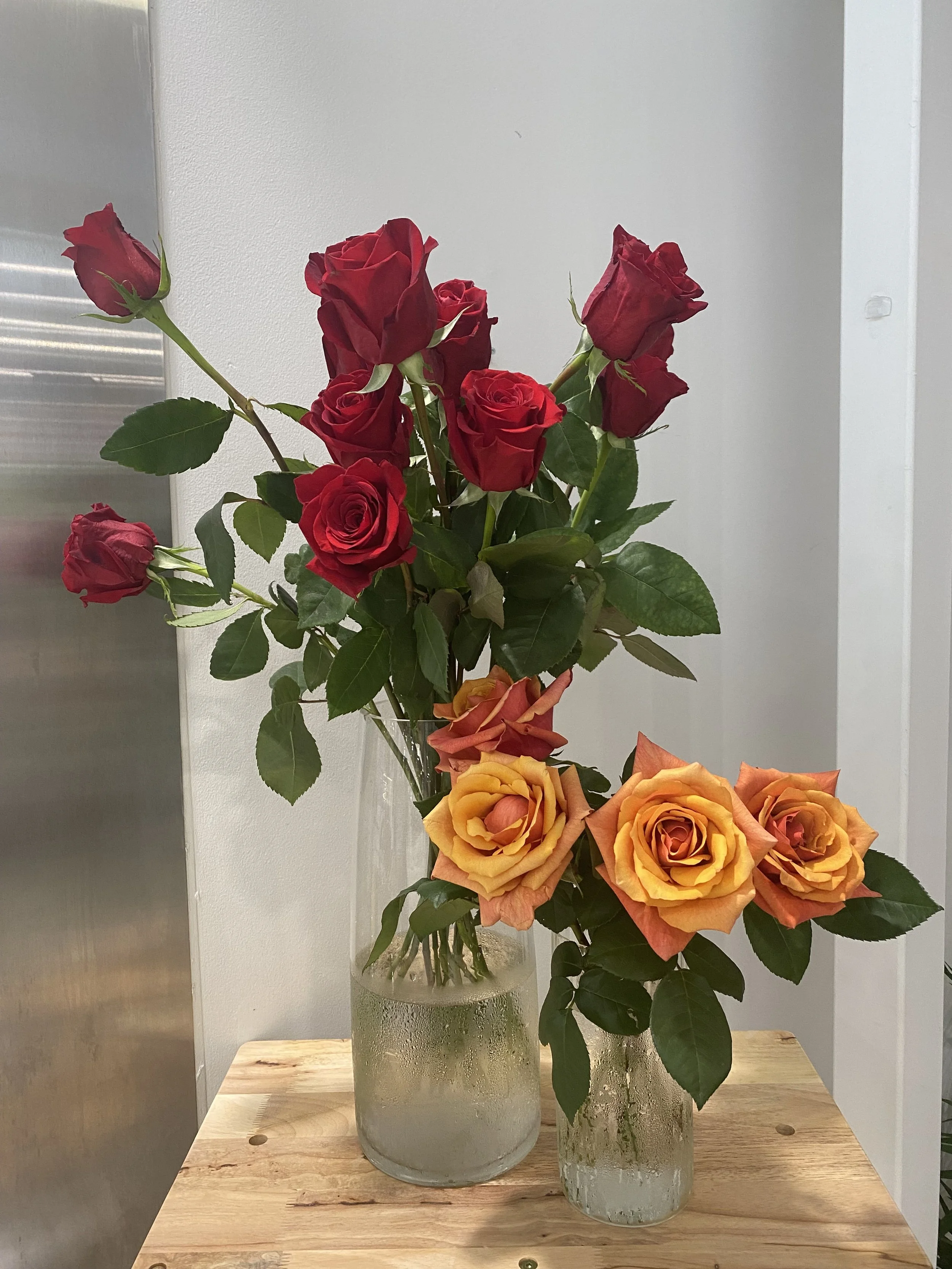 Two vases with red and orange roses sitting on a wooden table.