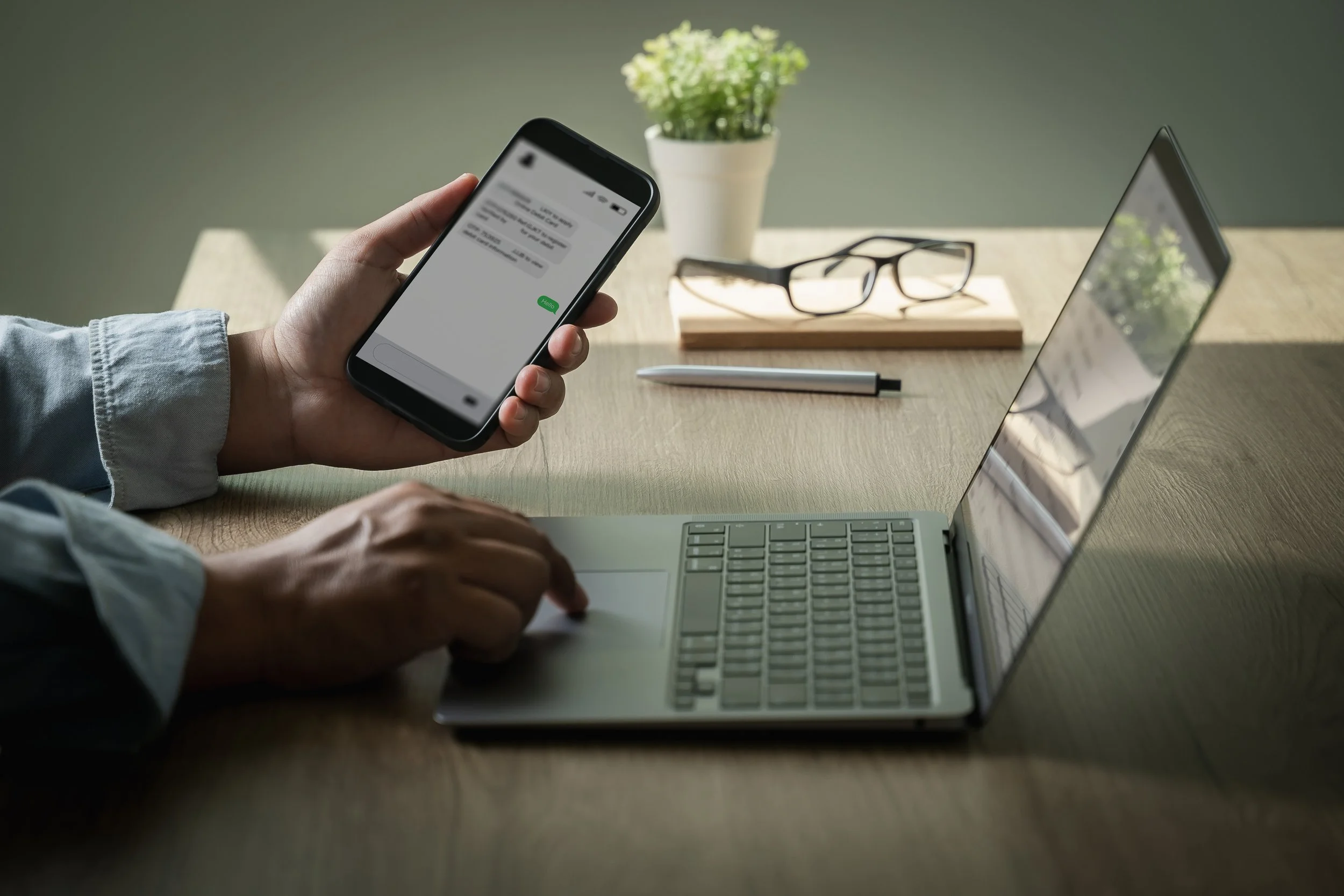 Mobiltelefon SMS foran laptop på pult med bok, pen, kaffekopp og briller