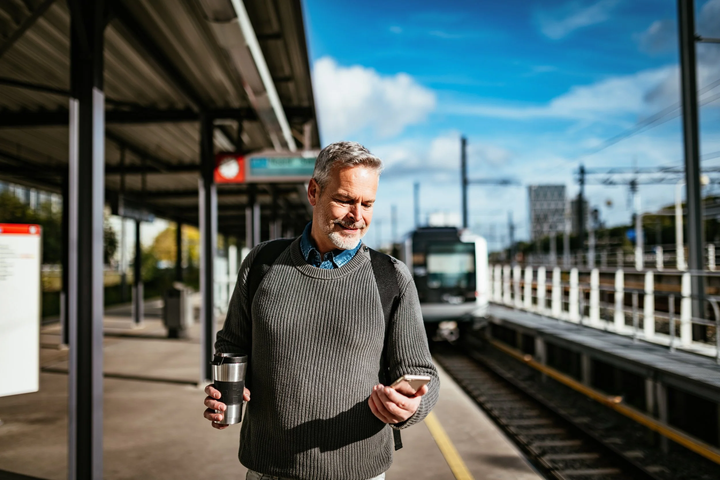 Mann som holder mobiltelefon på togstasjon eller tbane stopp