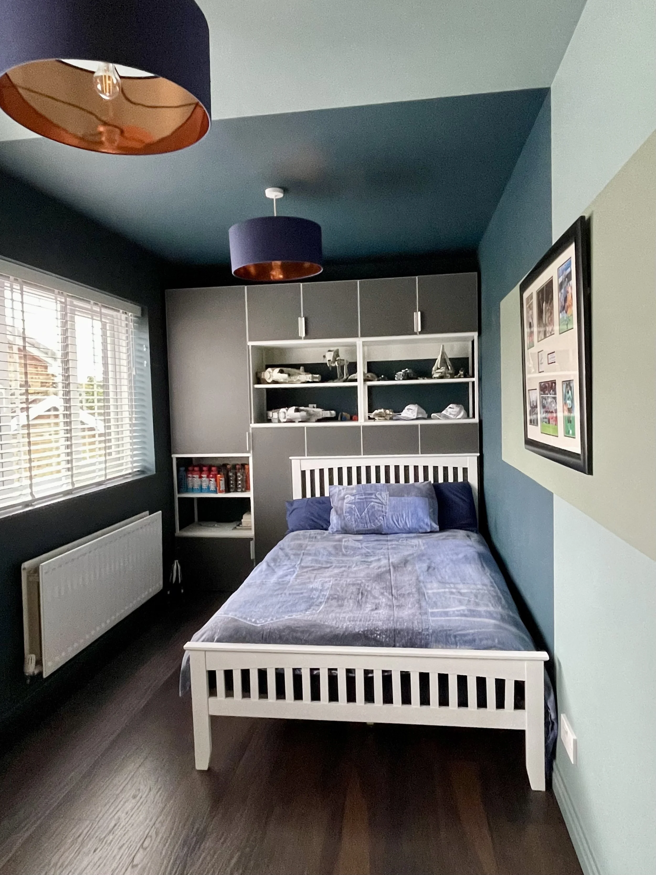 Boys' bedroom with navy and teal walls, white bed frame, built-in grey storage and framed football memorabilia wall art