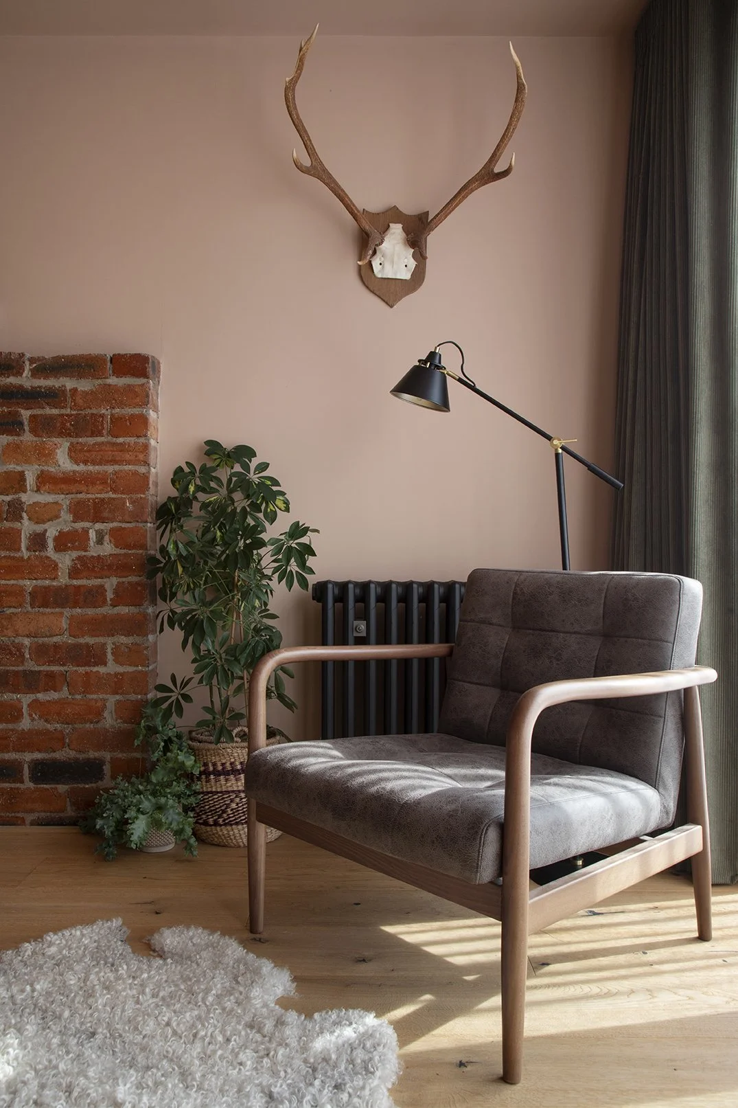 Loft bedroom sitting area in the Queens Road project by Carole Crowe Interior Design, Whitley Bay, featuring a mid-century style dark grey tufted armchair with walnut arms on wide plank light oak flooring, a black adjustable floor lamp, decorative an