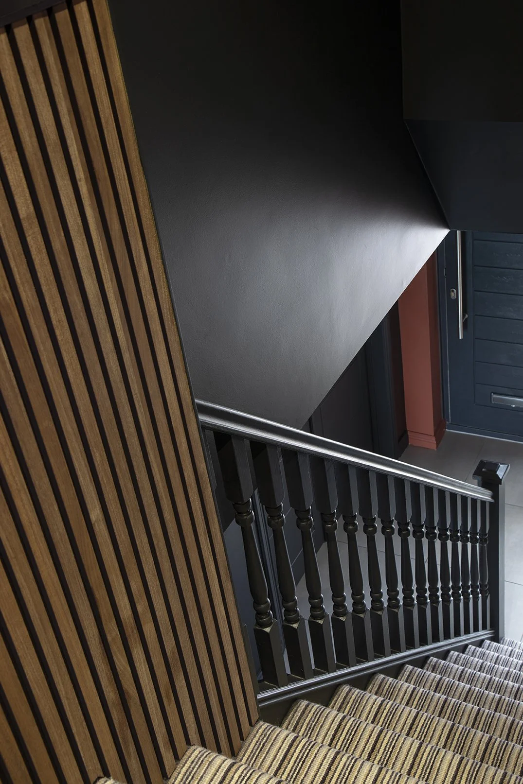 Detail shot looking down staircase with warm oak wood slat panel, painted black spindles and striped stair runner, Lytham Road