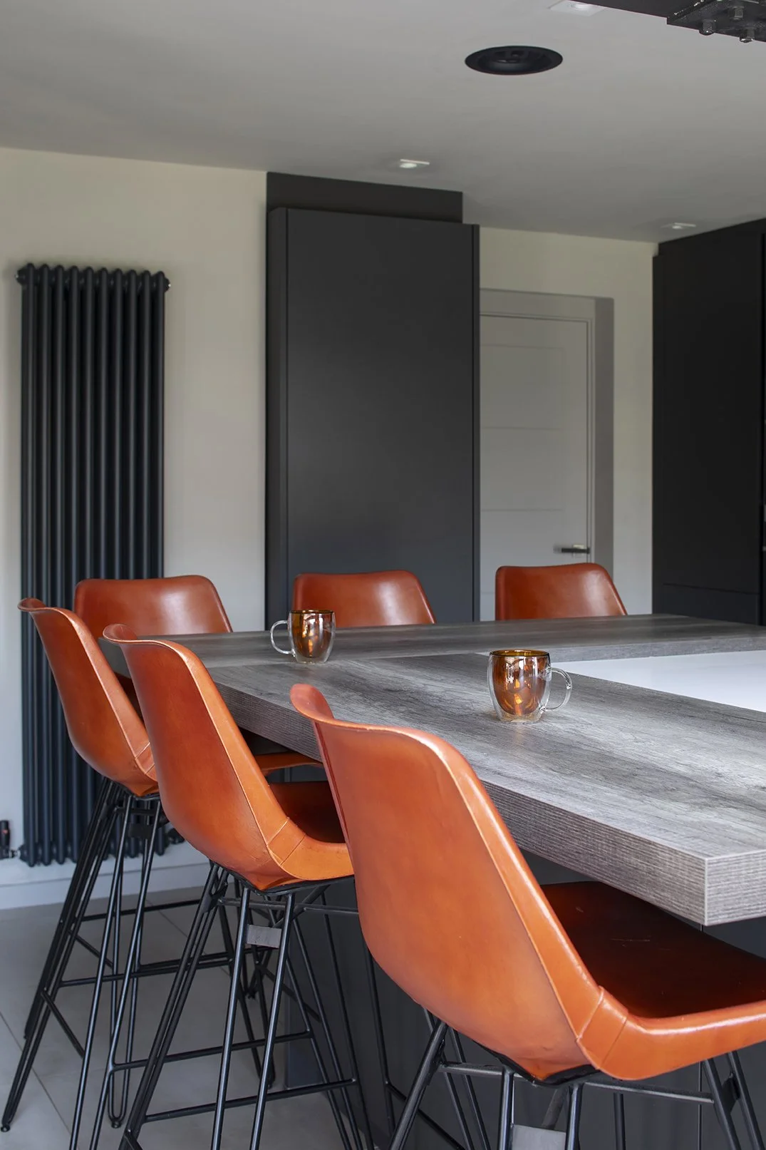 Close-up of tan leather bar stools at grey kitchen island with tall black column radiator, Lytham Road Whitley Bay