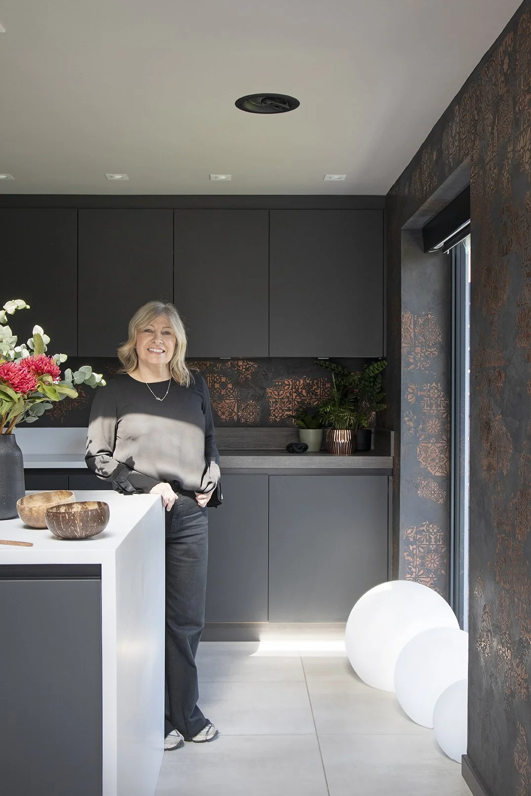 Interior designer Carole Crowe with client in dark kitchen beside black and copper Venetian plaster wall, Lytham Road Tynemouth