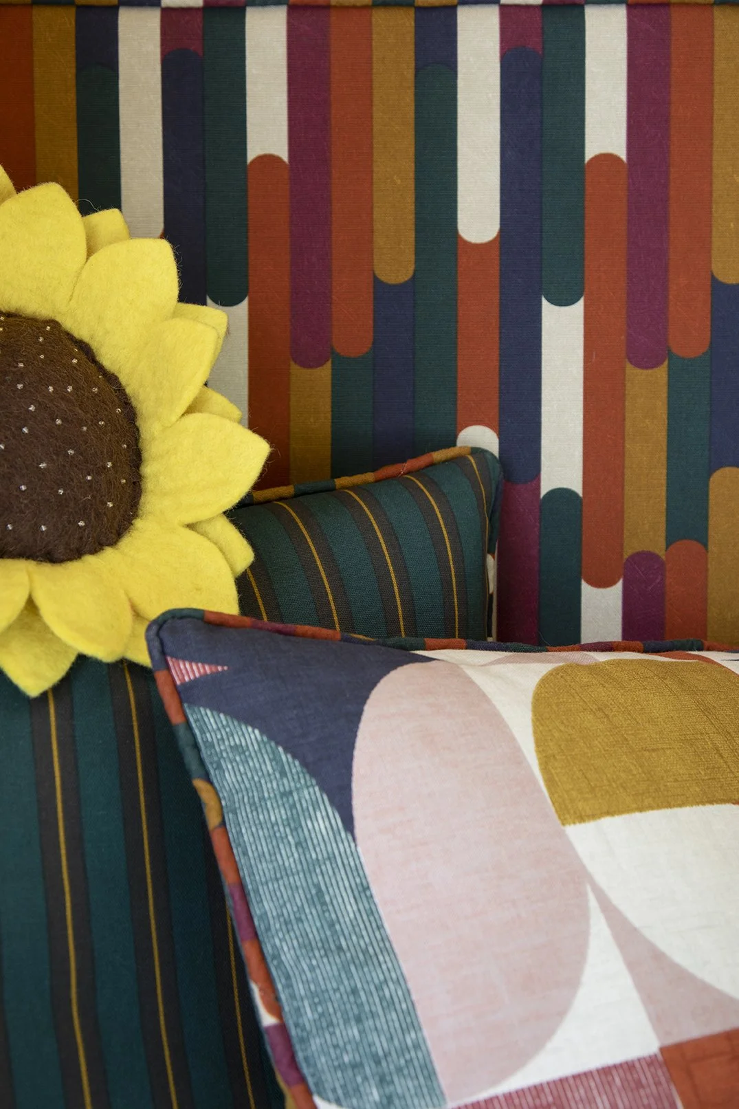 Fabric and cushion detail inside the built-in reading nook of a North Shields family home by Carole Crowe Interior Design, showing the bold multicoloured geometric stripe banquette upholstery, a dark teal and gold fine stripe scatter cushion, a large