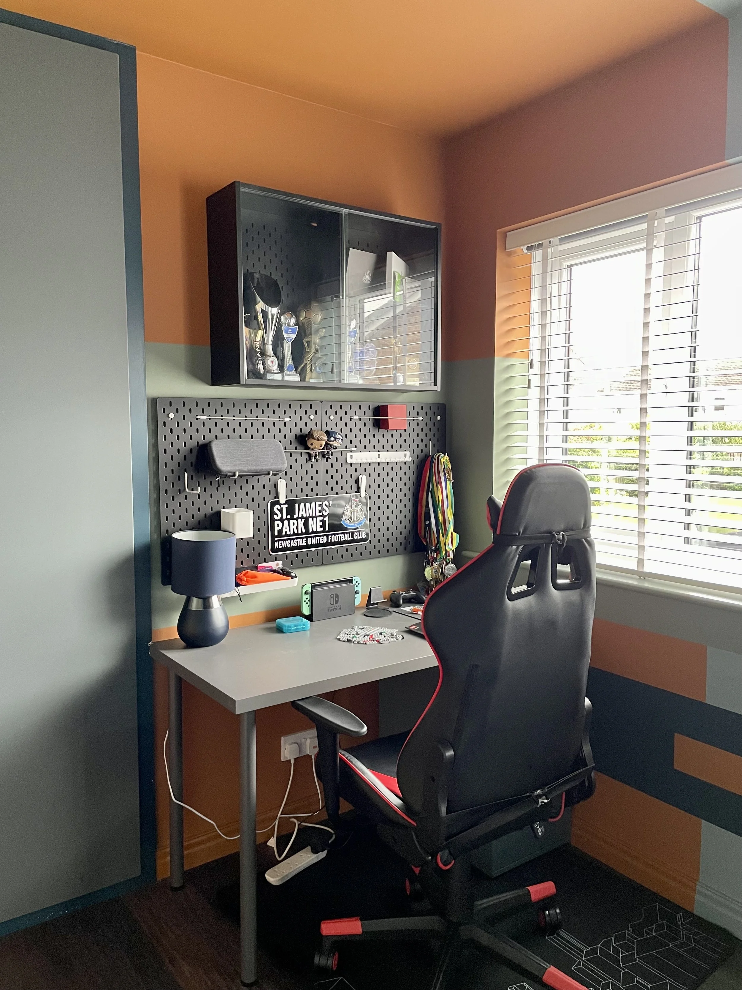 Boys' bedroom desk area with Newcastle United St James' Park sign, gaming chair, pegboard and trophy display cabinet