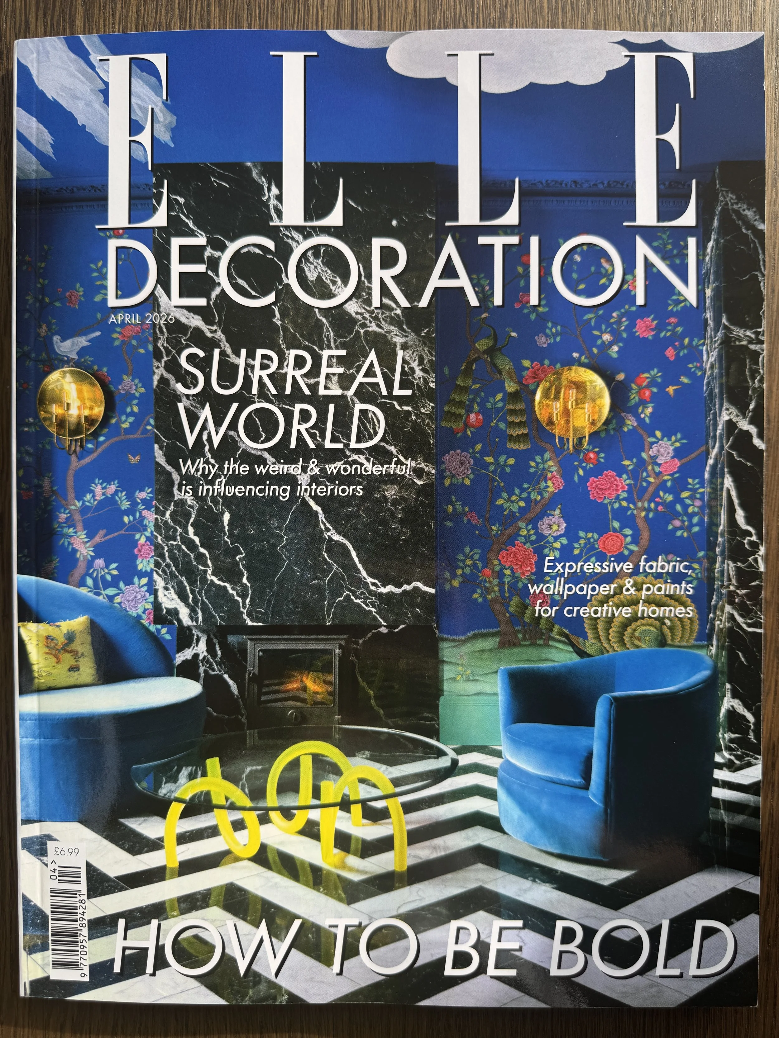 A magazine cover titled "Elle Decoration" featuring a vibrant, surreal interior space with colorful wallpaper, velvet chairs, a fireplace, and striking yellow furniture accents.