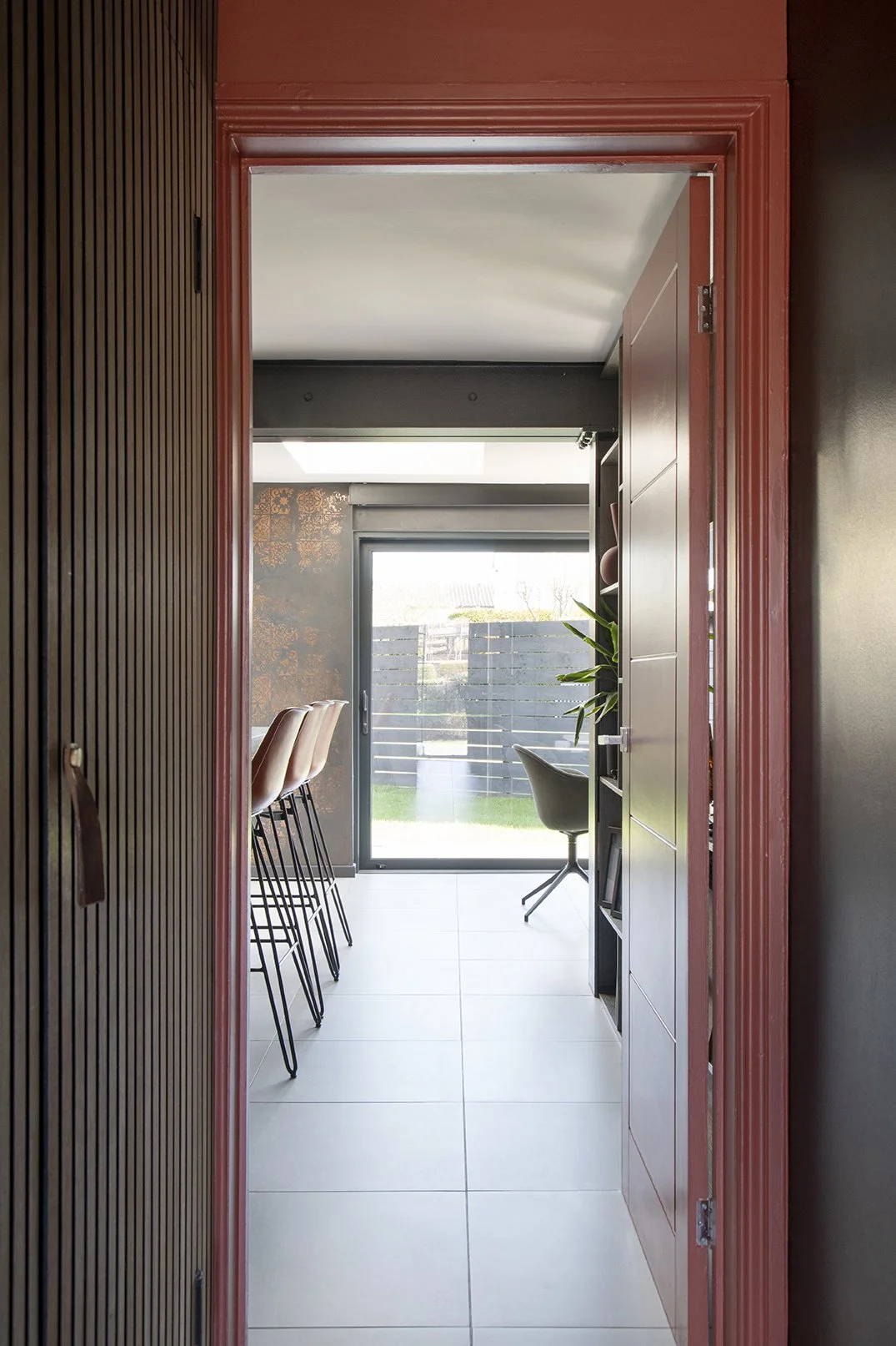 View from hallway through terracotta painted doorframe into bright open-plan kitchen extension with copper Venetian plaster walls and garden beyond, Lytham Road Whitley Bay