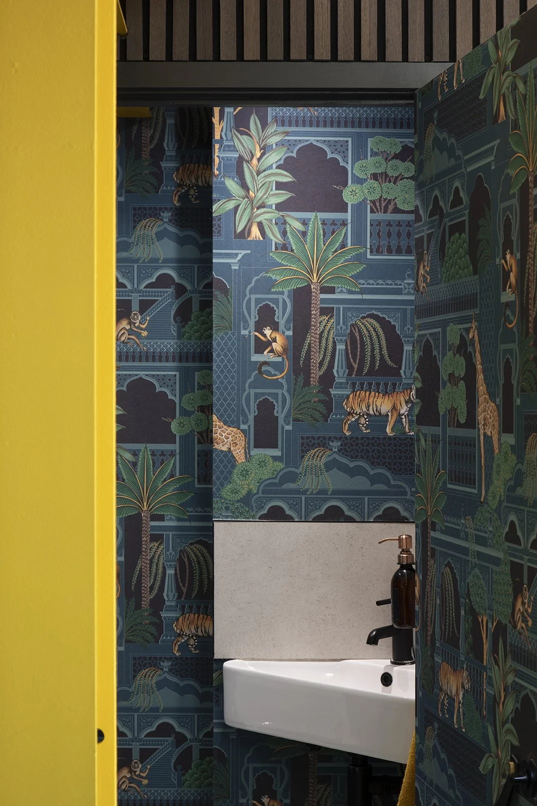 Downstairs cloakroom in a North Shields family home designed by Carole Crowe Interior Design, with dramatic floor-to-ceiling jungle print wallpaper featuring tigers, giraffes, monkeys and tropical palms within Mughal-inspired arched architecture in d