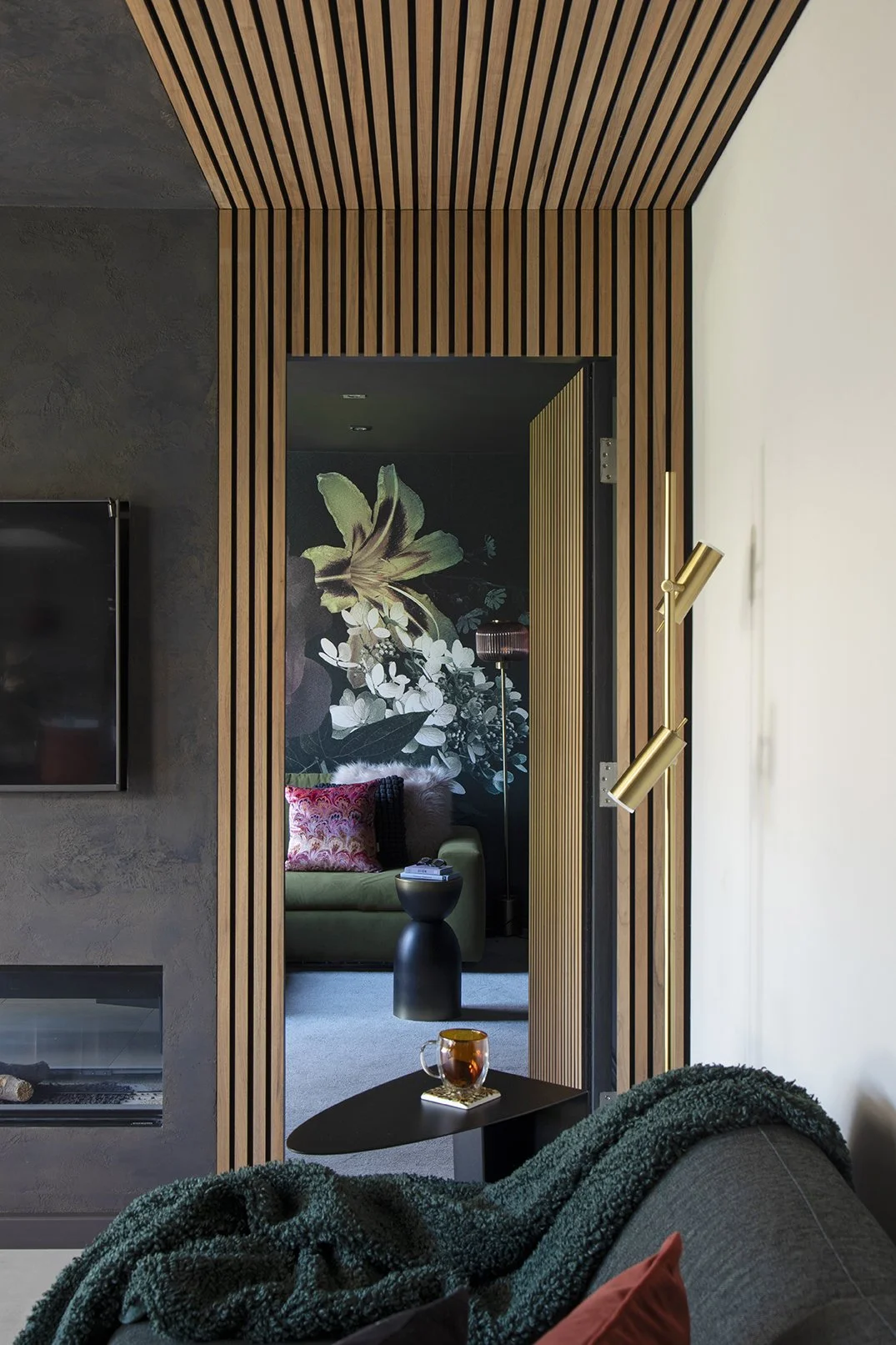 View from living room through open oak wood slat concealed snug door revealing dark botanical floral mural and olive sofa beyond, Lytham Road Tynemouth
