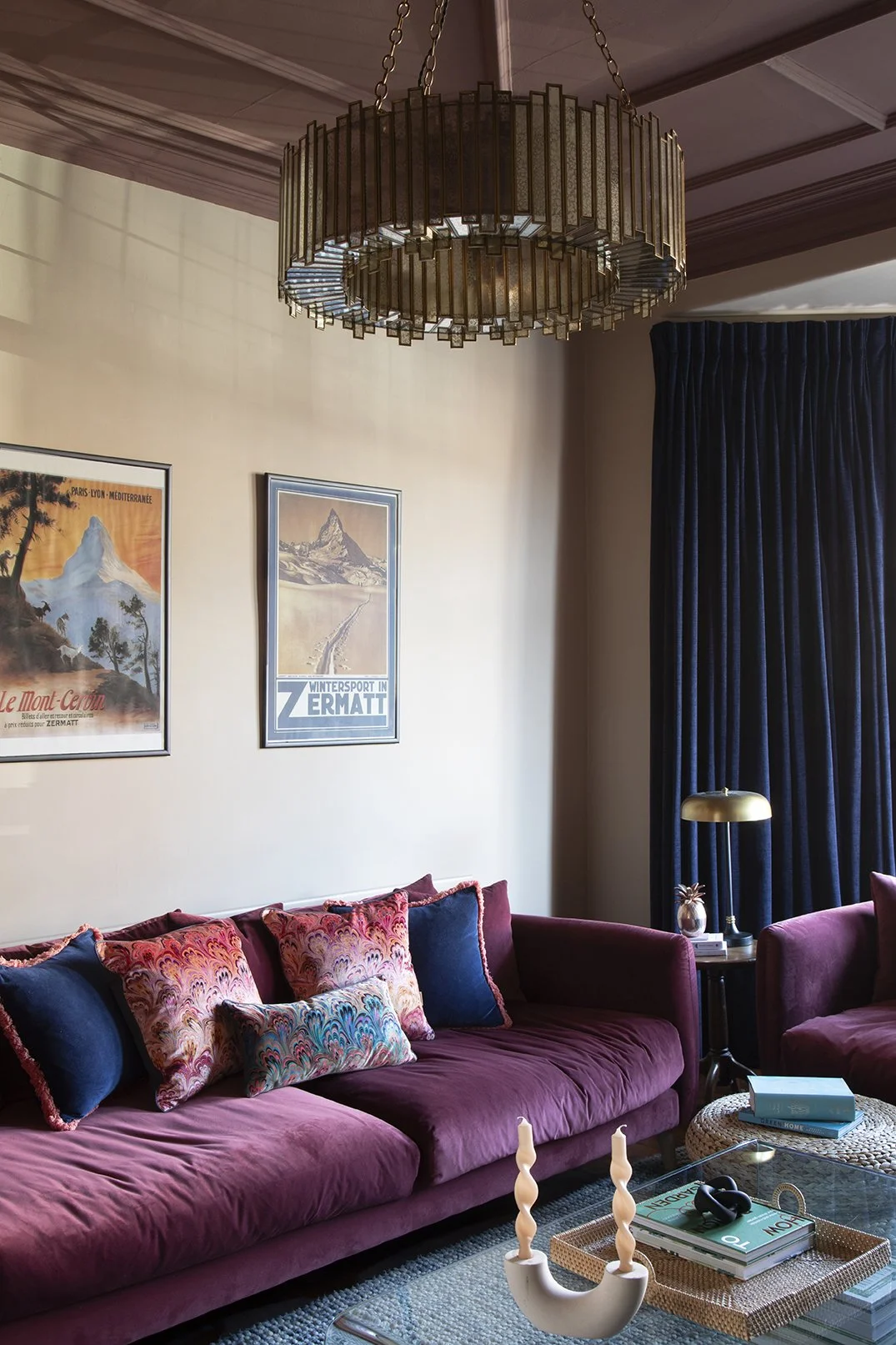 Overview of the sitting room in the Queens Road project by Carole Crowe Interior Design, Whitley Bay, featuring a large plum velvet sofa with multicoloured marbled print and navy cushions, a brass and smoked glass drum chandelier above an ornate plum