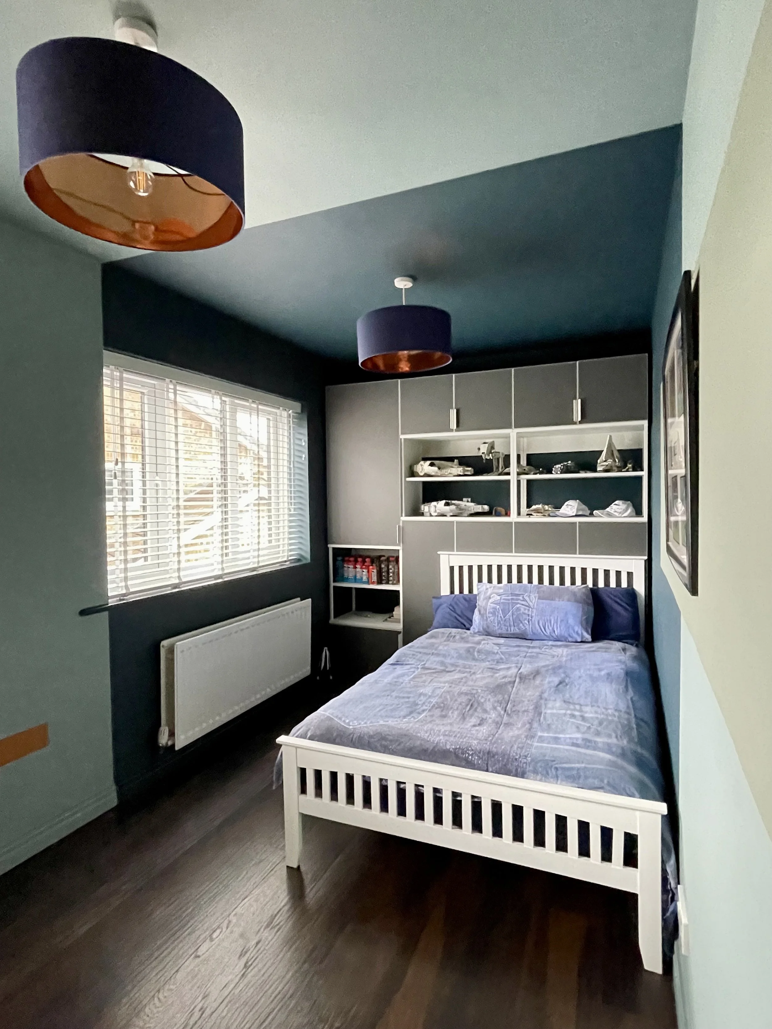 Boys' bedroom with dark navy and teal colour-blocked walls, white wooden bed frame and copper-lined drum pendant lights