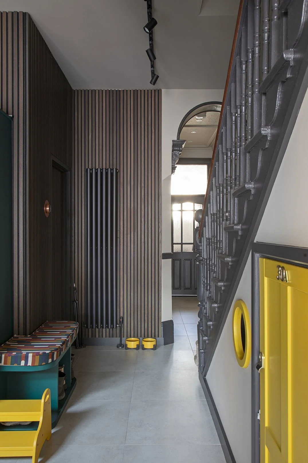  Hallway and boot room zone in a North Shields family home designed by Carole Crowe Interior Design, featuring a teal painted storage bench with colourful striped upholstered seat cushion and open shoe storage below, a dark timber slatted wall panel 