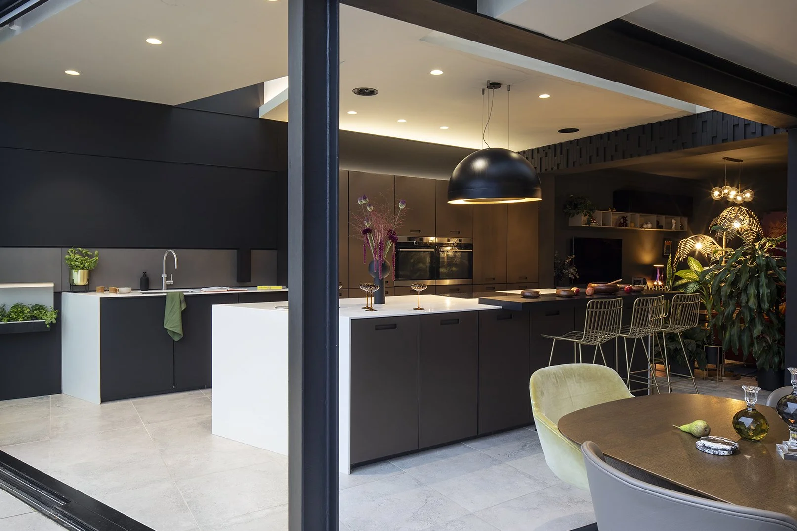 Dark kitchen viewed from garden with angled island, black dome pendant light, brass wire bar stools and warm accent lighting, Queens Road Whitley Bay